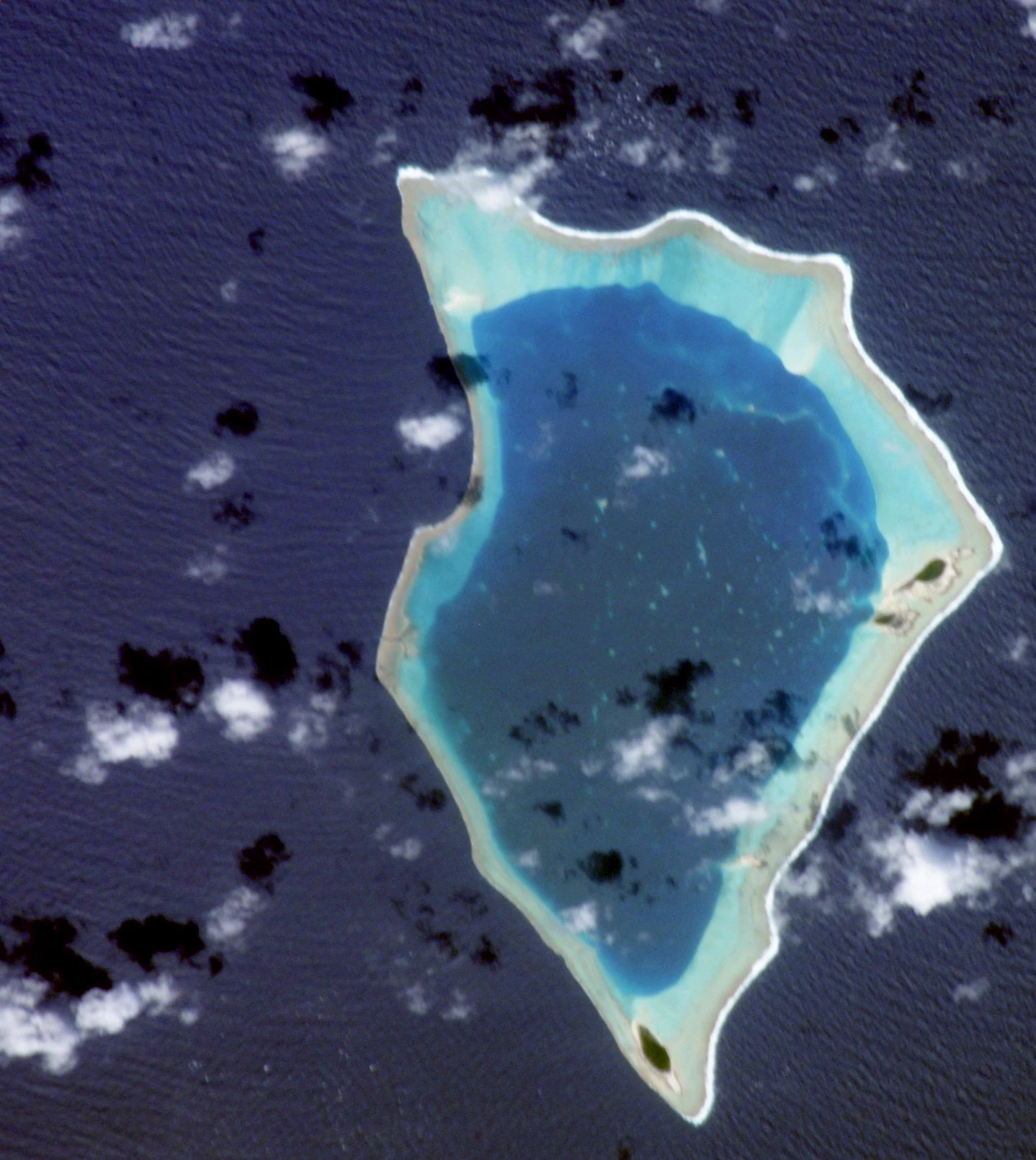 Satellite aerial view of Bikar Atoll, showing a coral reef ring surrounding a central lagoon, set against the dark blue Pacific Ocean.