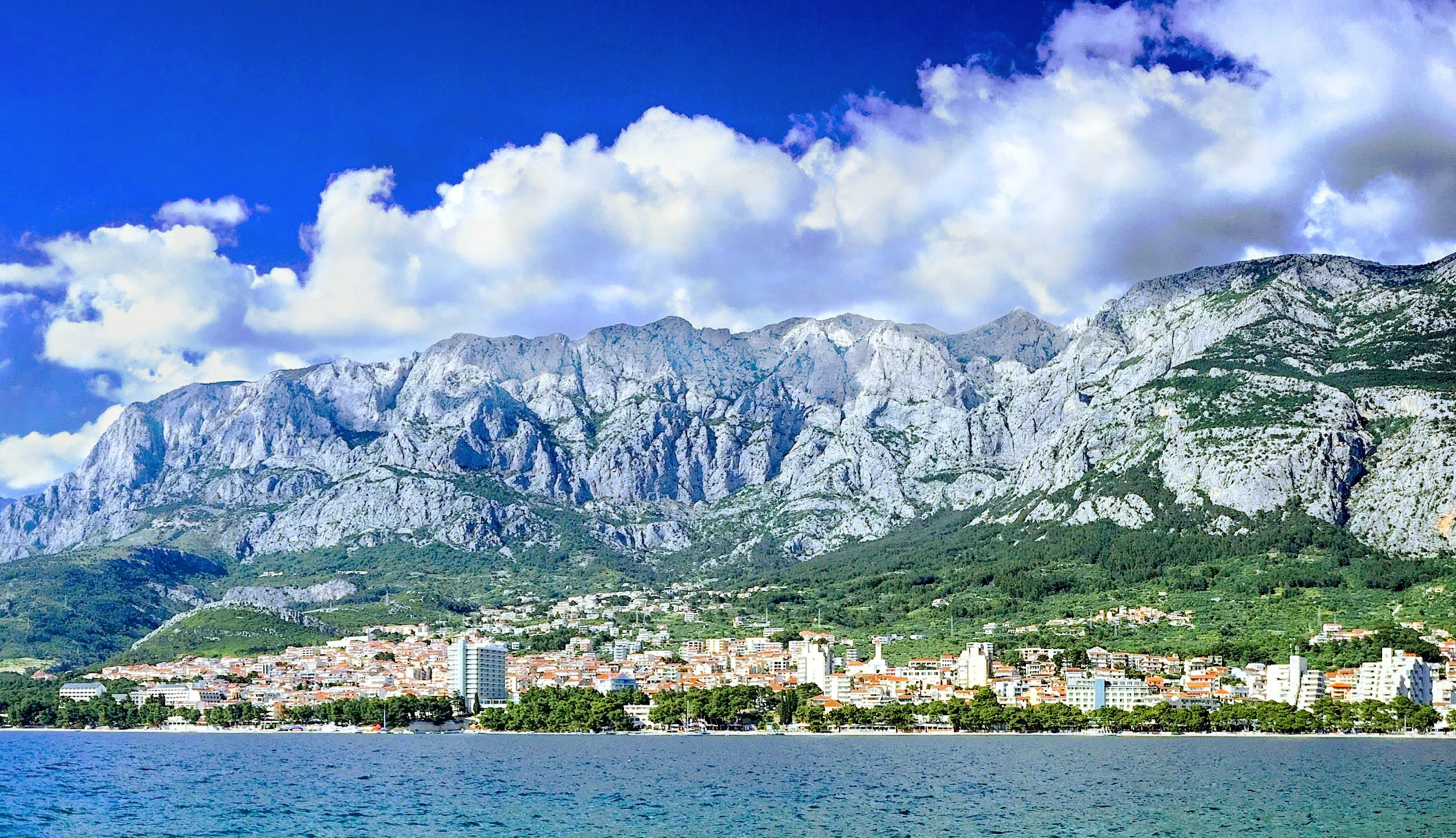 Panoramic view of Biokovo mountain range with Makarska town and the Adriatic Sea under a blue sky with scattered clouds