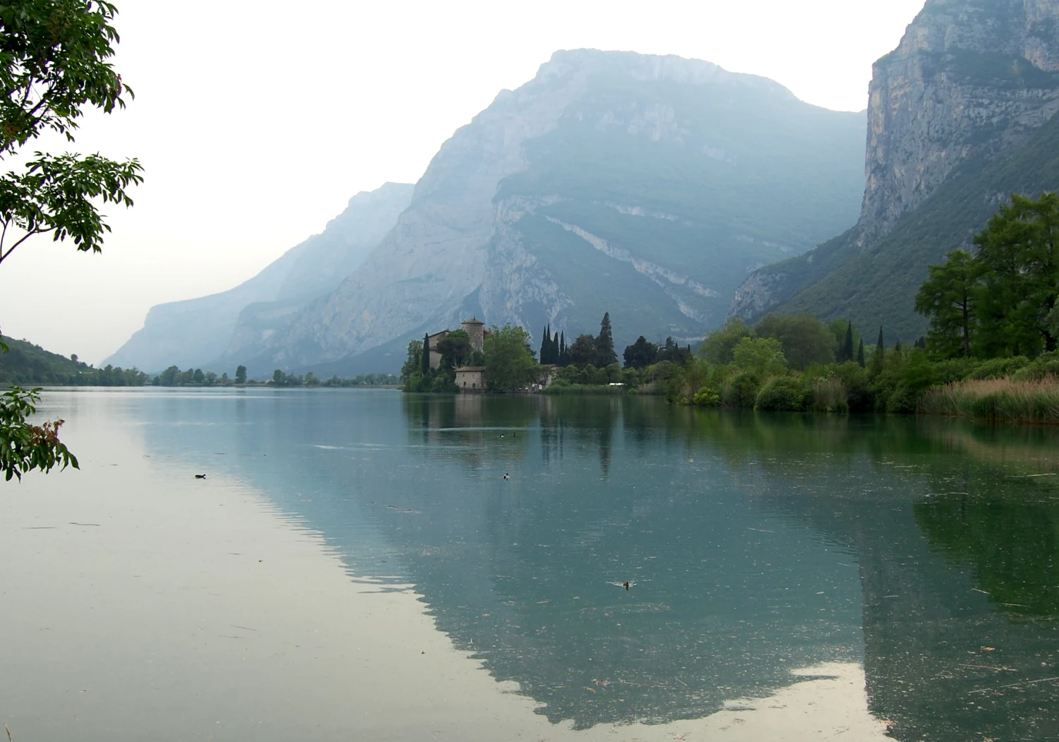 Un lago tranquilo que refleja las montañas circundantes y una pequeña estructura de castillo en la península lejana.