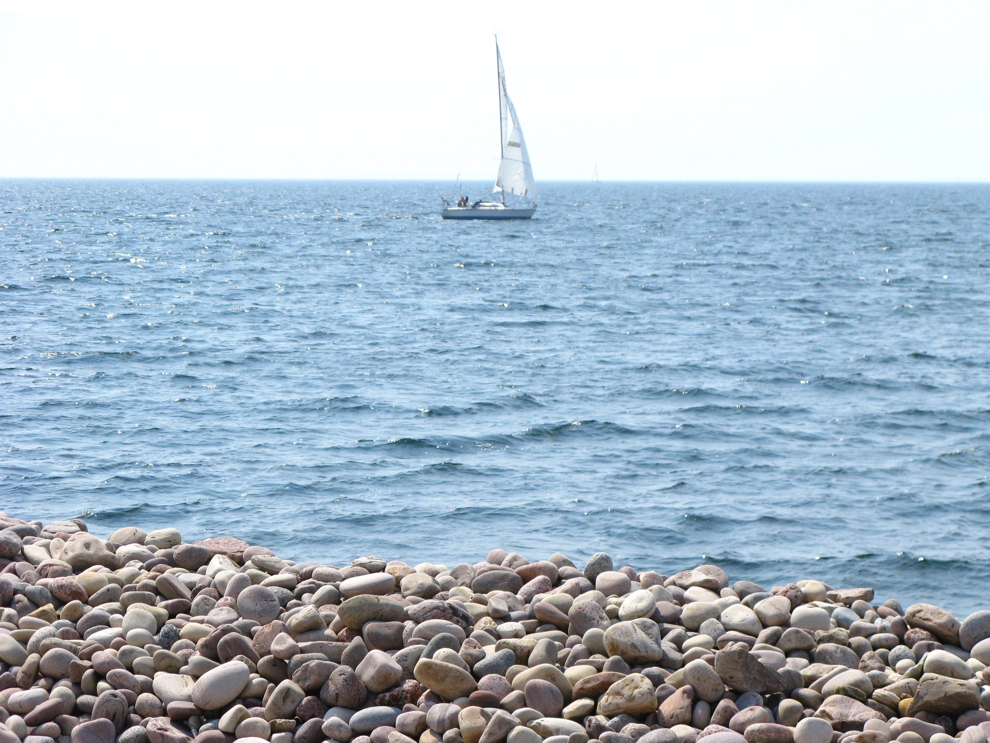 Rocky beach with a sailboat on the ocean horizon