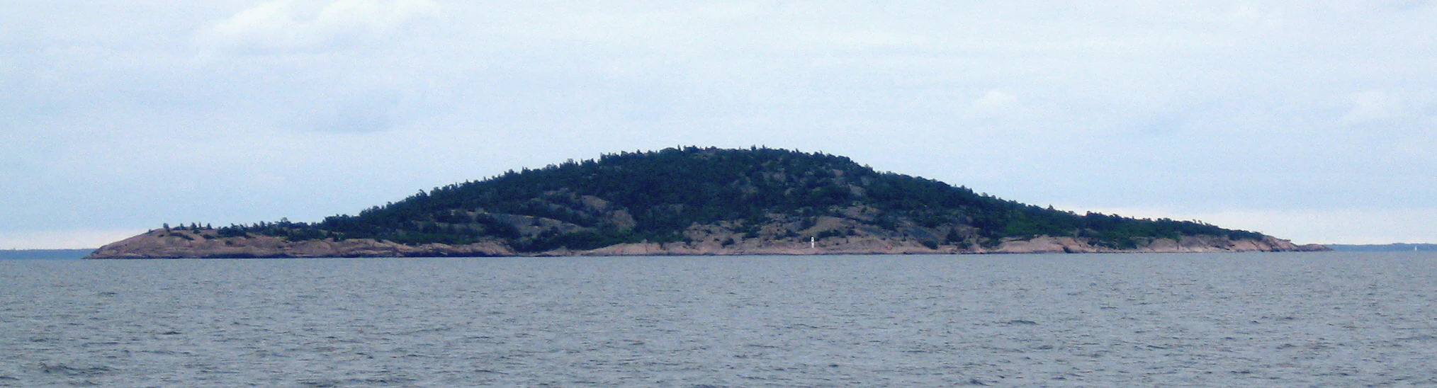 Blå Jungfrun island with forested hills surrounded by water under a cloudy sky
