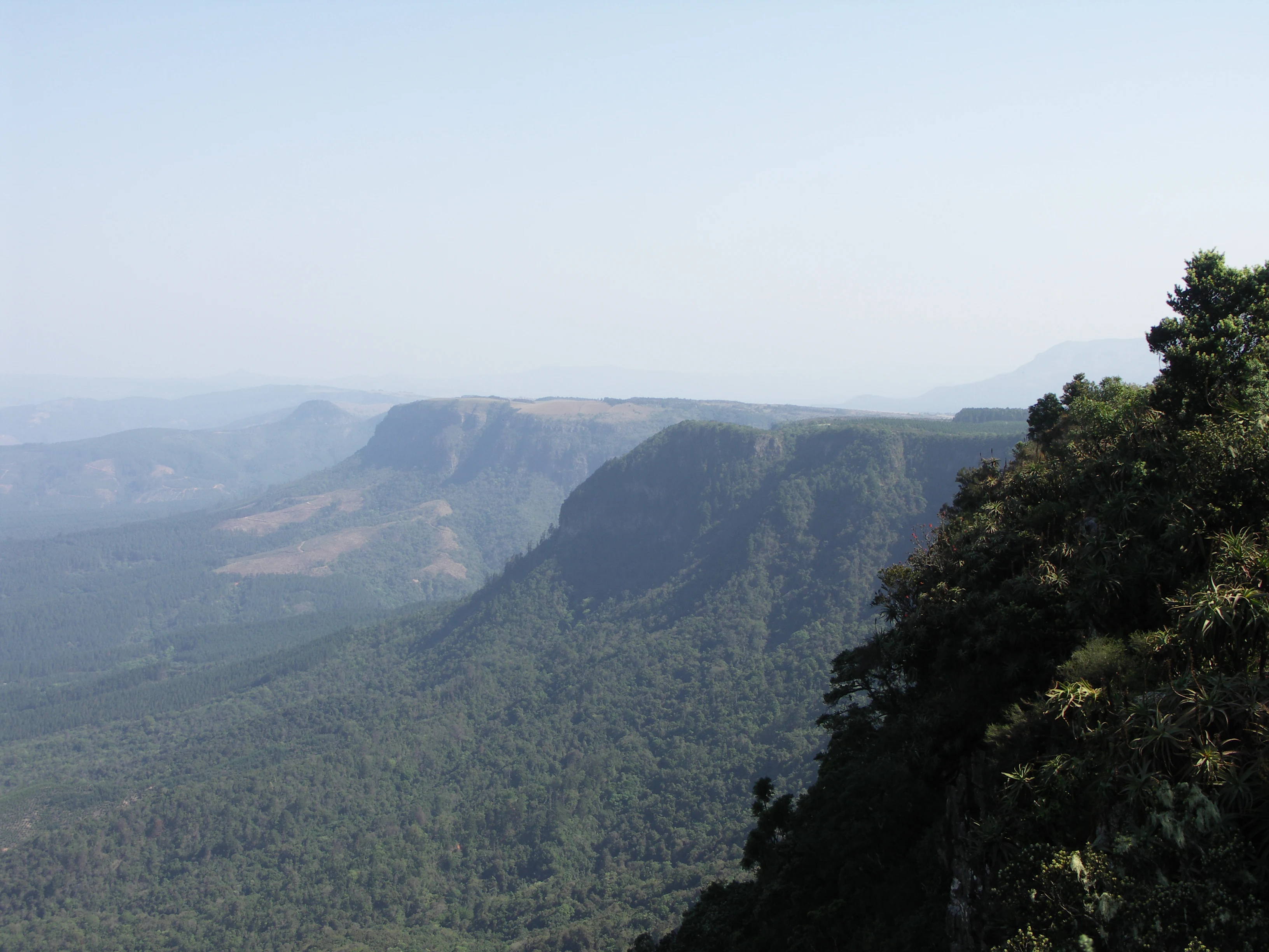 A hazy, panoramic view of forested mountain ridges and valleys extending into the distance from a high vantage point.