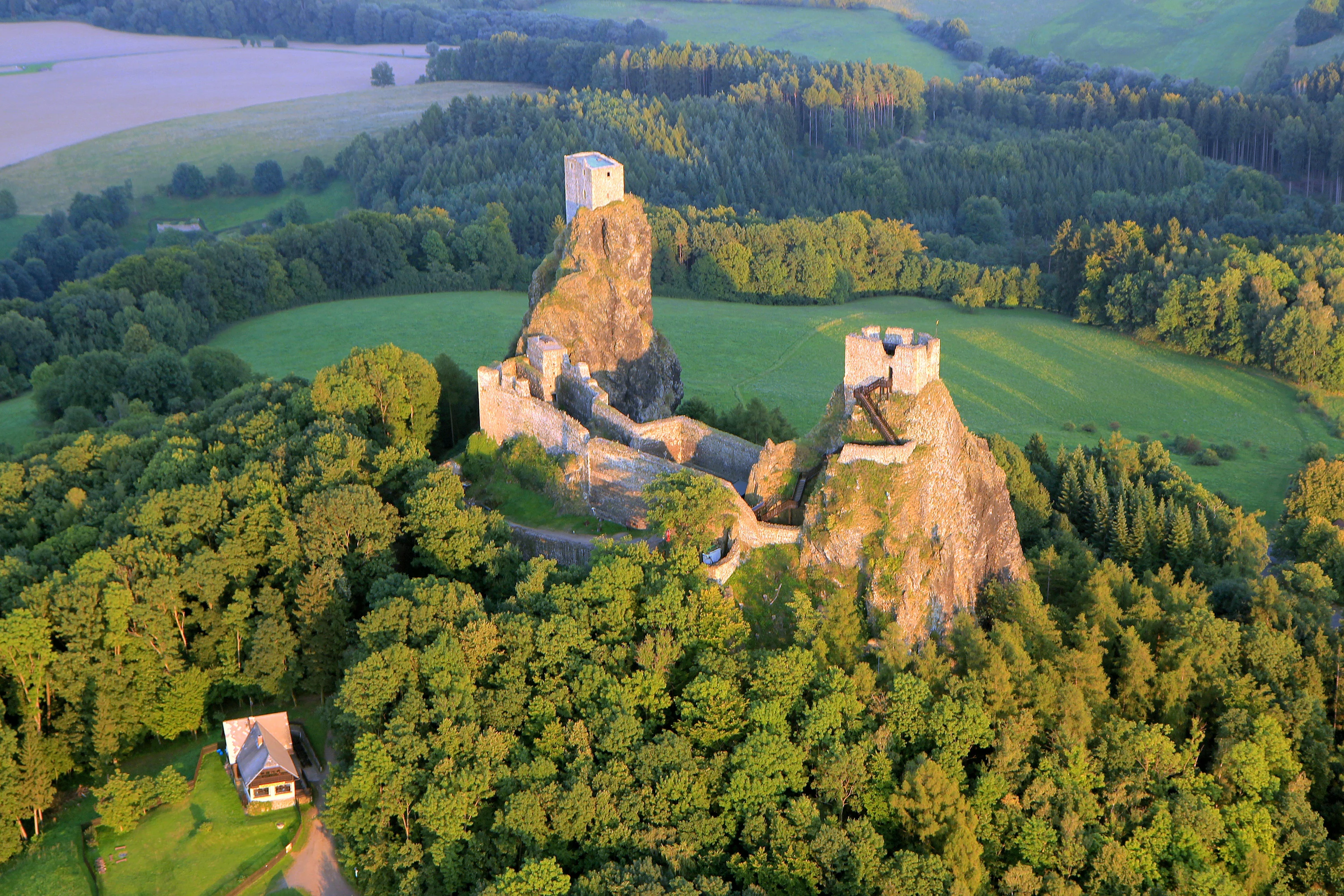 Aerial view of Trosky Castle on rocky cliffs surrounded by green forest and fields