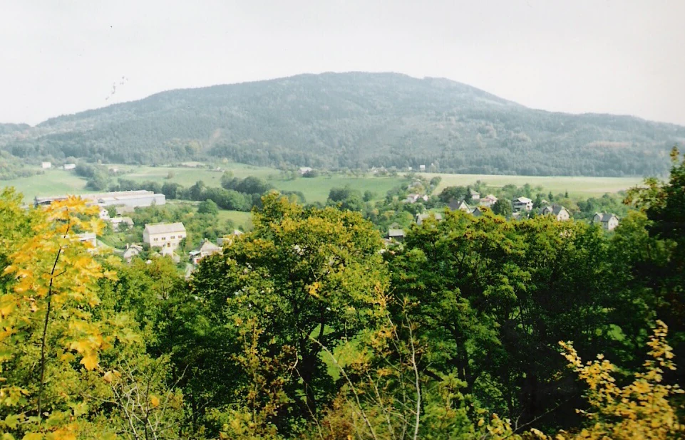 Kozákov mountain visible in the distance with green forest and valley settlements under an overcast sky