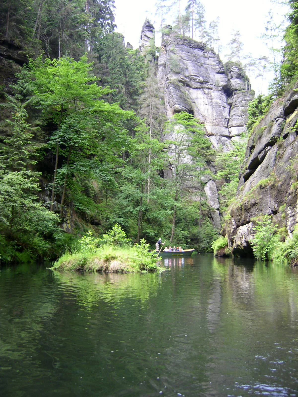 River flowing through narrow gorge with green trees, steep rock cliffs, and small boat on water