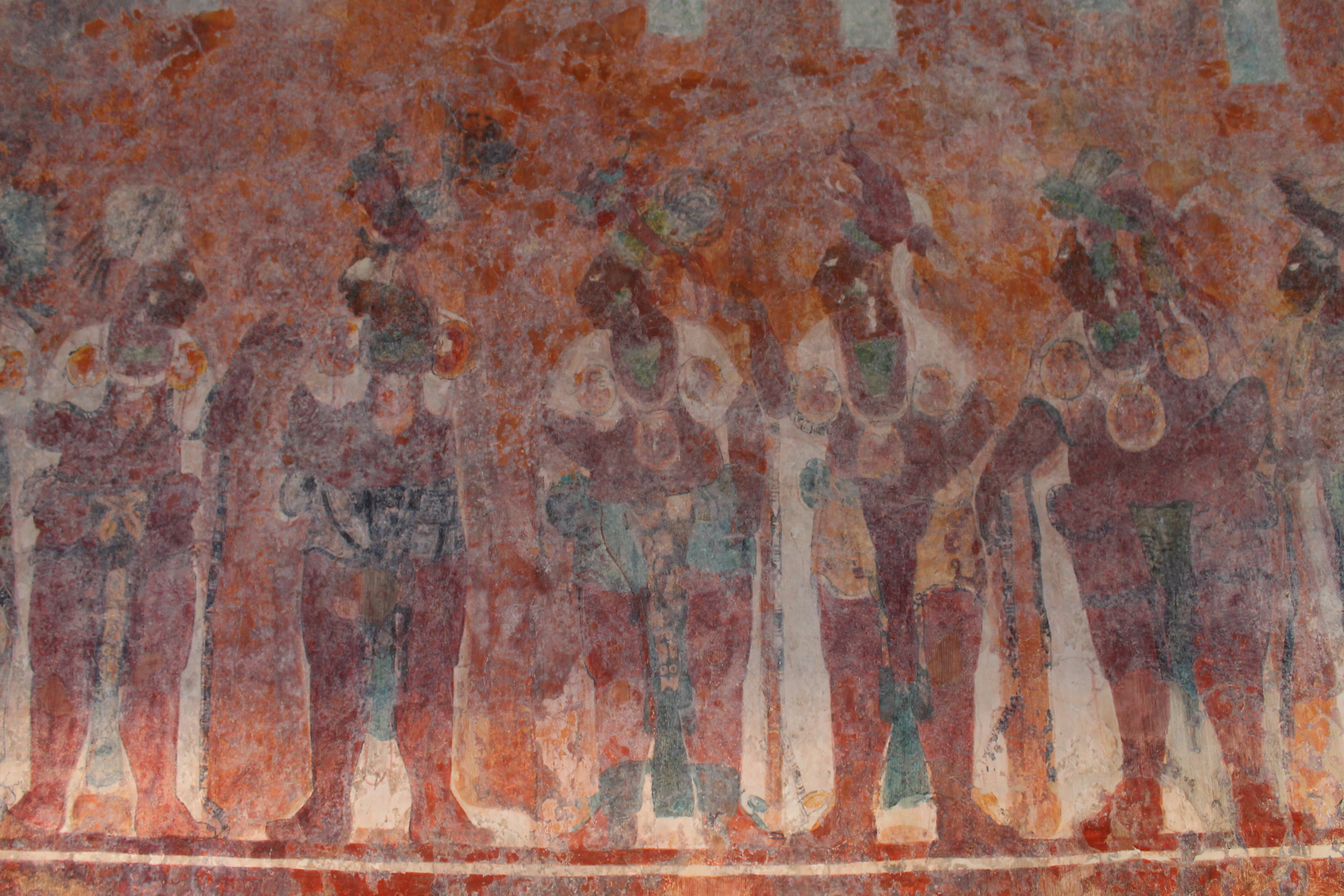 Faded ancient Maya wall paintings showing a group of figures in traditional attire standing in a row.