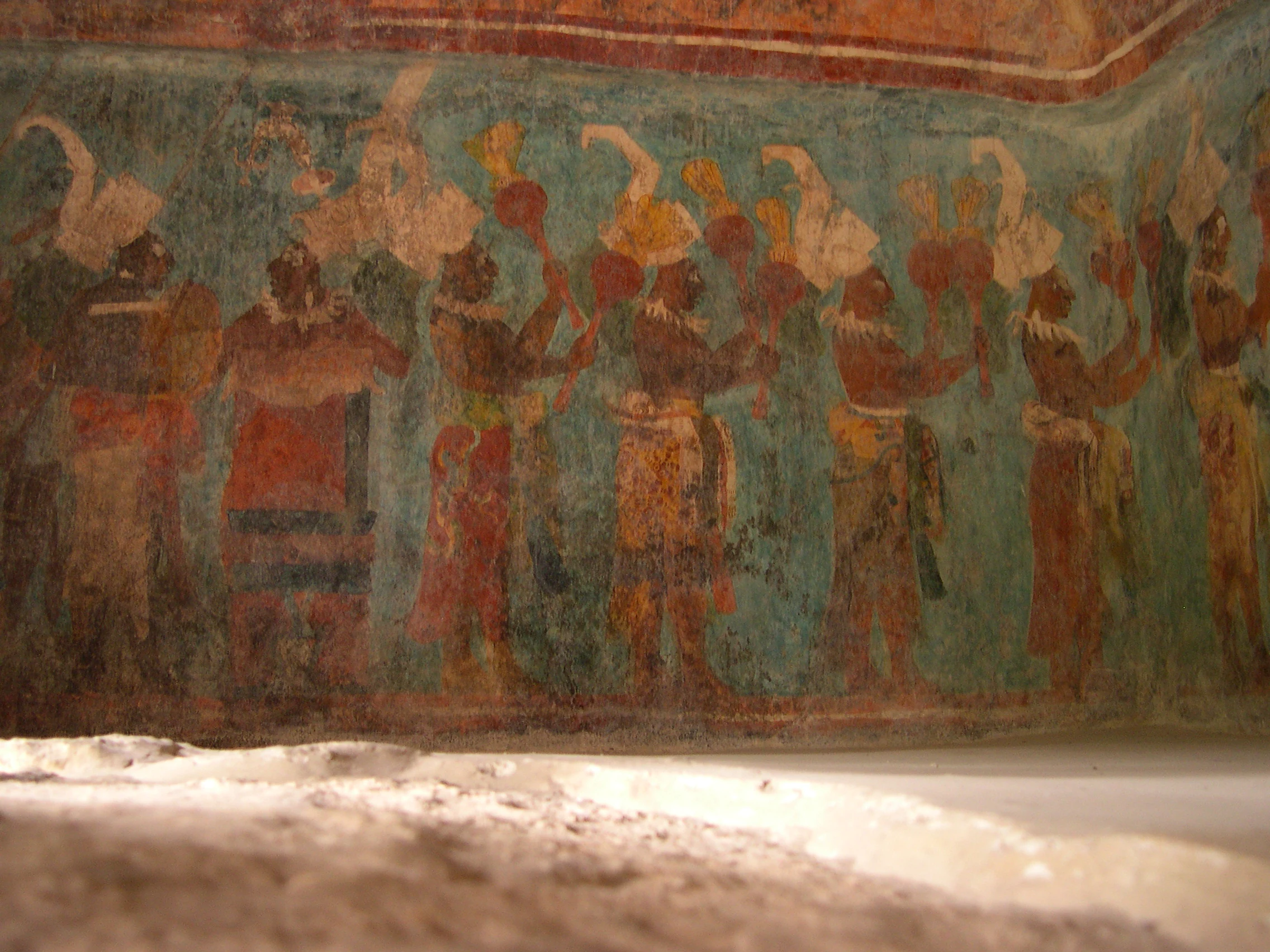 Ancient Maya mural painting depicting a procession of figures wearing elaborate headpieces against a faded teal background.