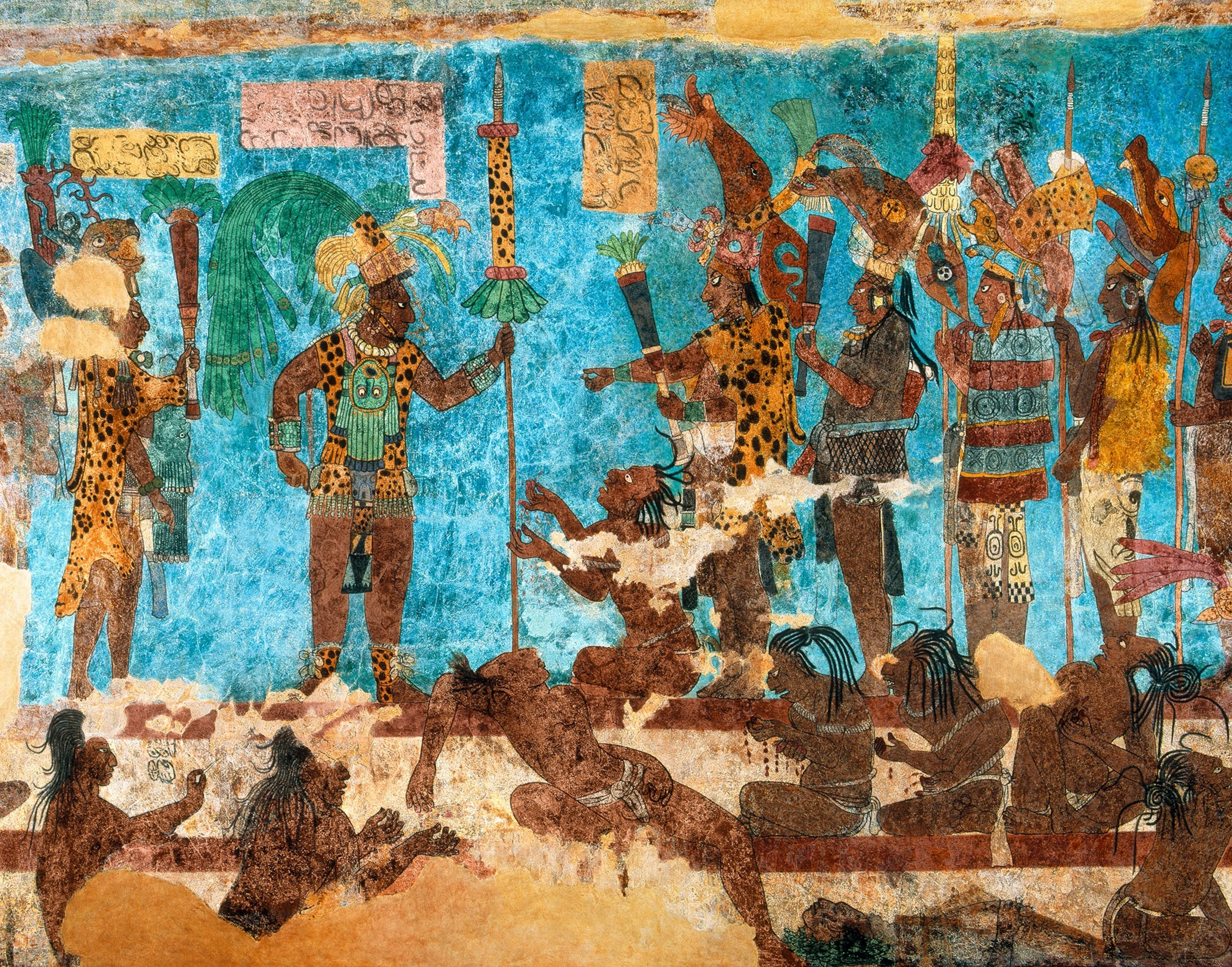 A vibrant ancient Mayan mural showing a group of people, including nobles wearing leopard skin patterned clothing and elaborate headdresses, standing and kneeling against a bright blue painted wall.