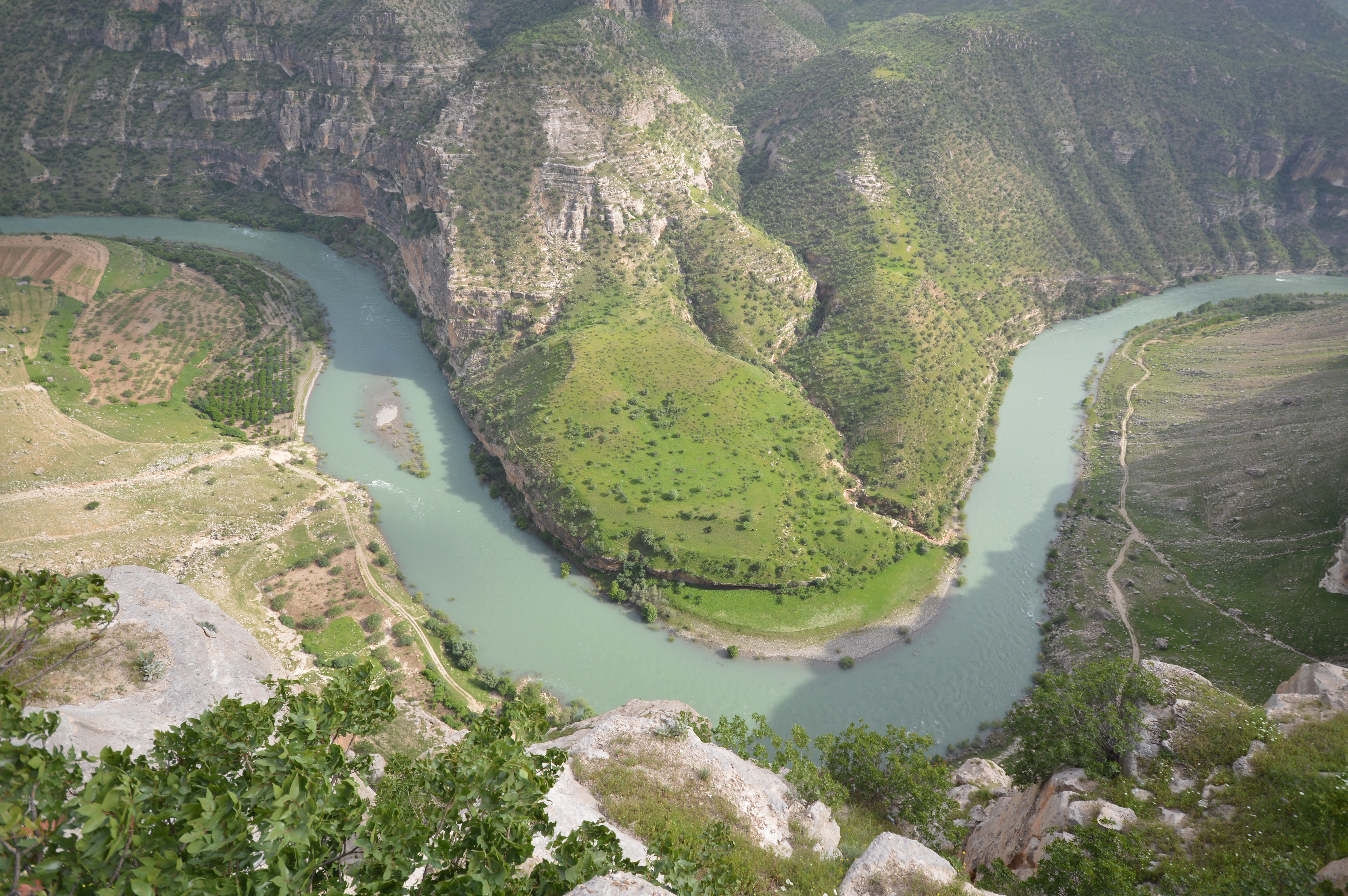 Aerial view of a winding river forming a U-shape through a mountainous valley with green slopes and rocky cliffs