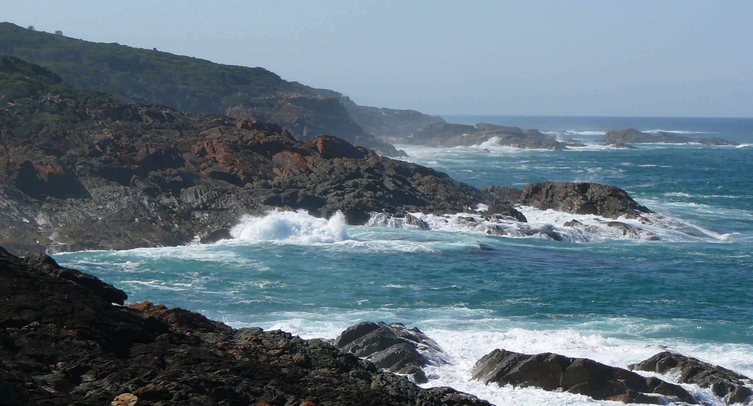 Rocky coastline with waves crashing against cliffs under a clear sky