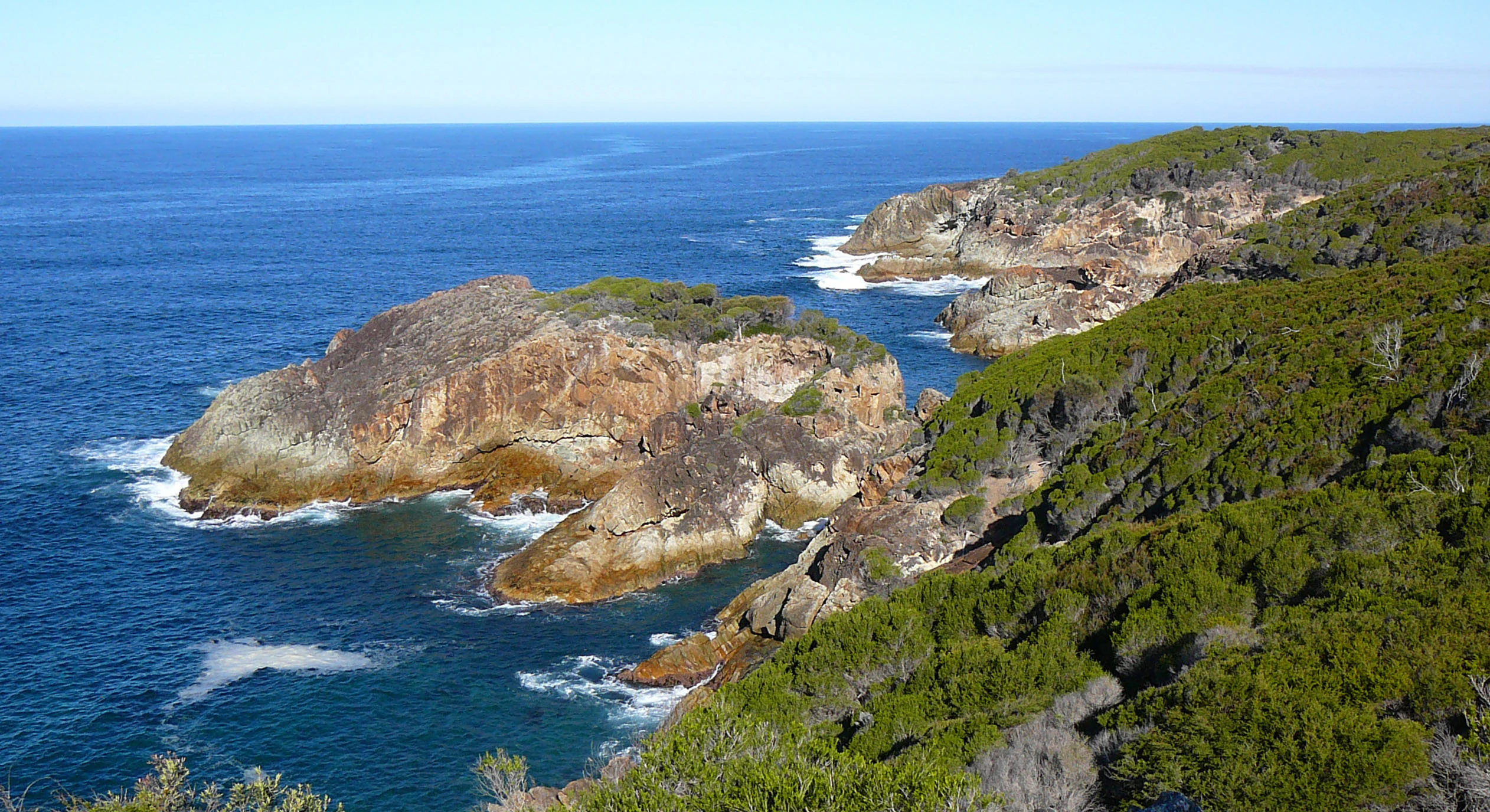 Coastal cliffs and ocean with green vegetation, viewed from above Kianinny Bay
