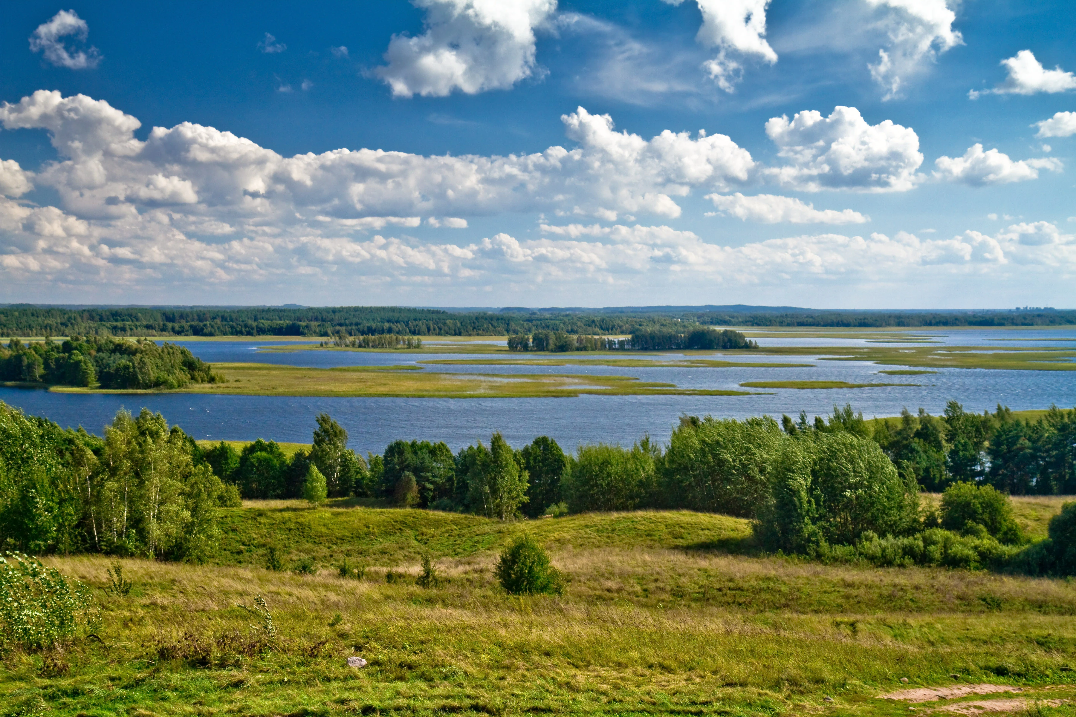 Wide landscape of Strusta Lake with green fields and forests under a partly cloudy sky