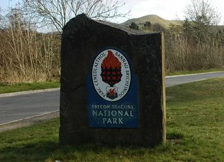 Stone sign with circular emblem and text 'Brecon Beacons National Park' on grassy roadside