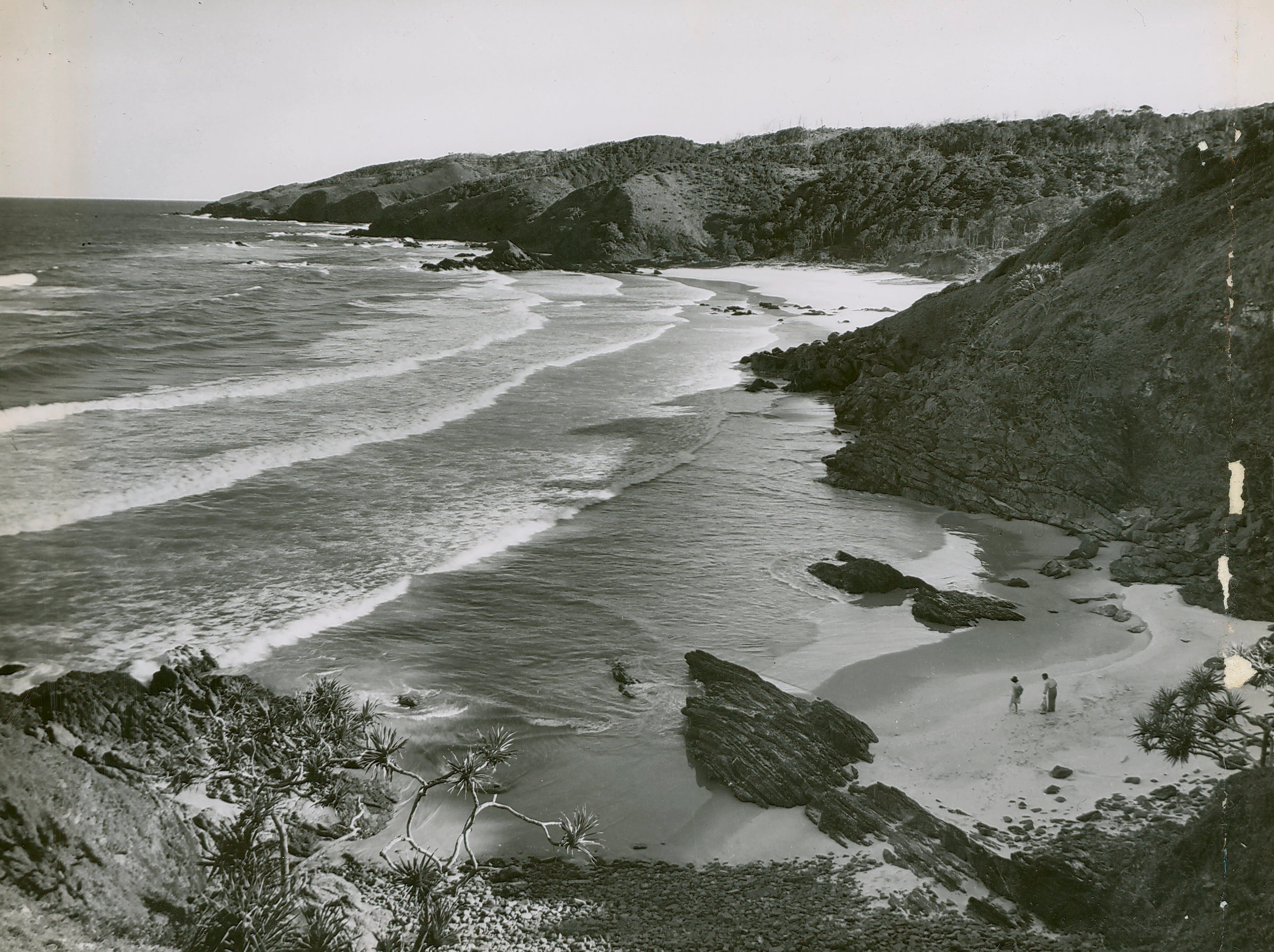 Black and white historical photograph looking down a rugged coastline towards a small beach and headland in New South Wales, Australia.