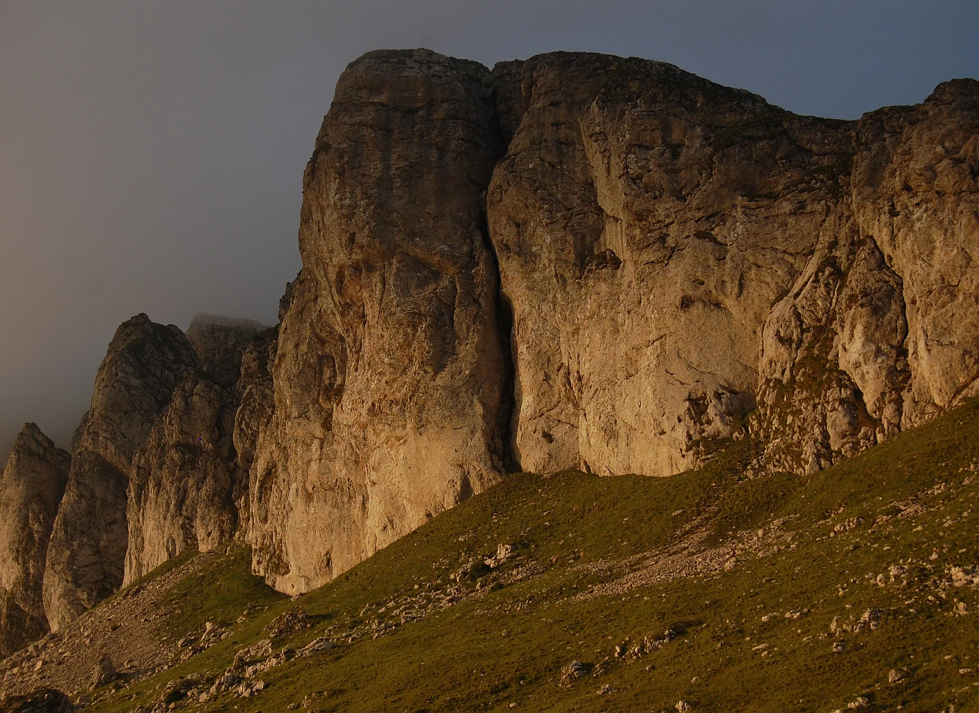 Rugged rock formations with grassy slopes under a muted sky in Bucegi Natural Park