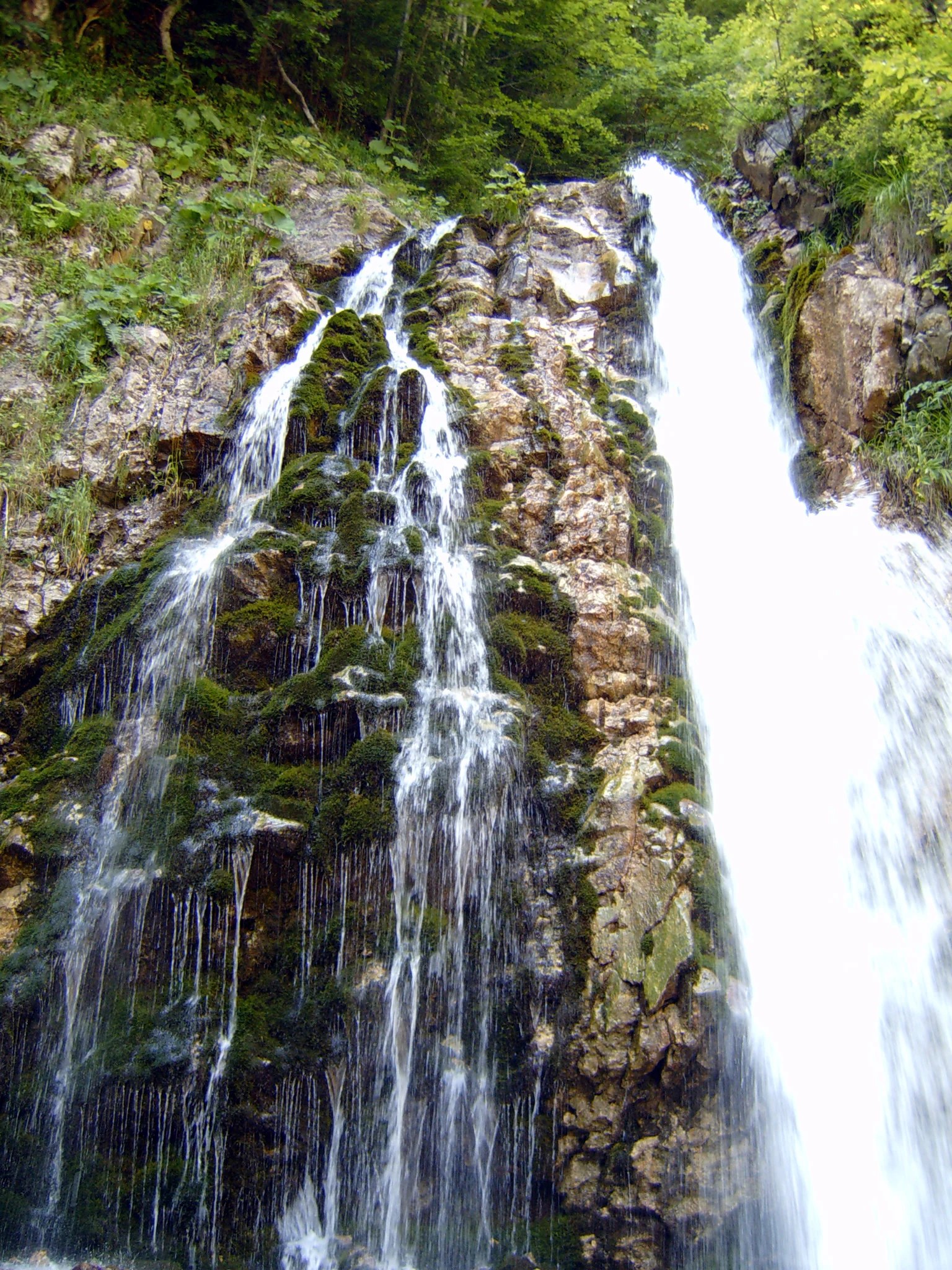 Waterfall flowing down rocky cliff face with moss-covered rocks and green vegetation