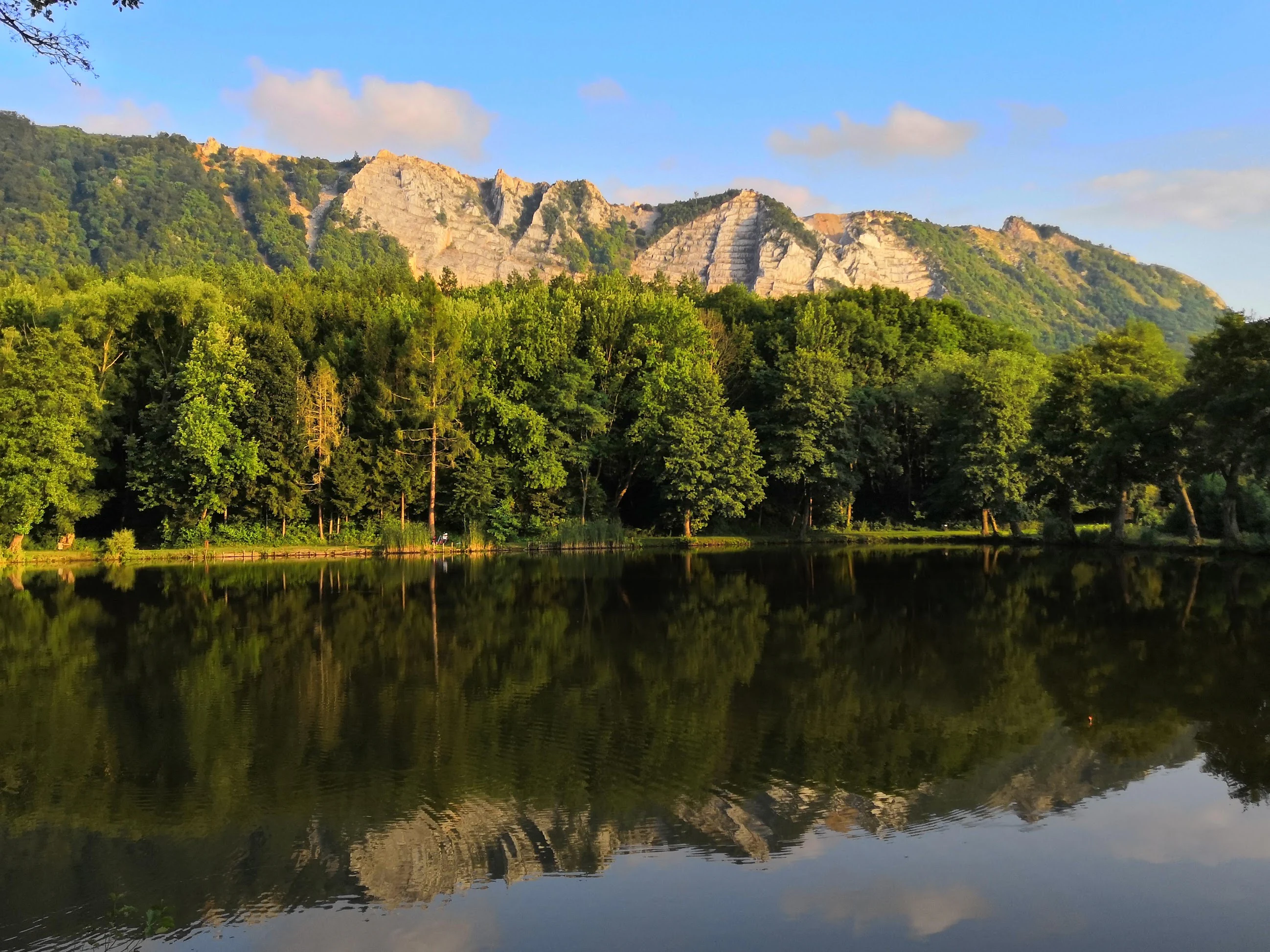 Lake Bélapátfalva reflecting forested mountains and rocky cliffs under a clear blue sky