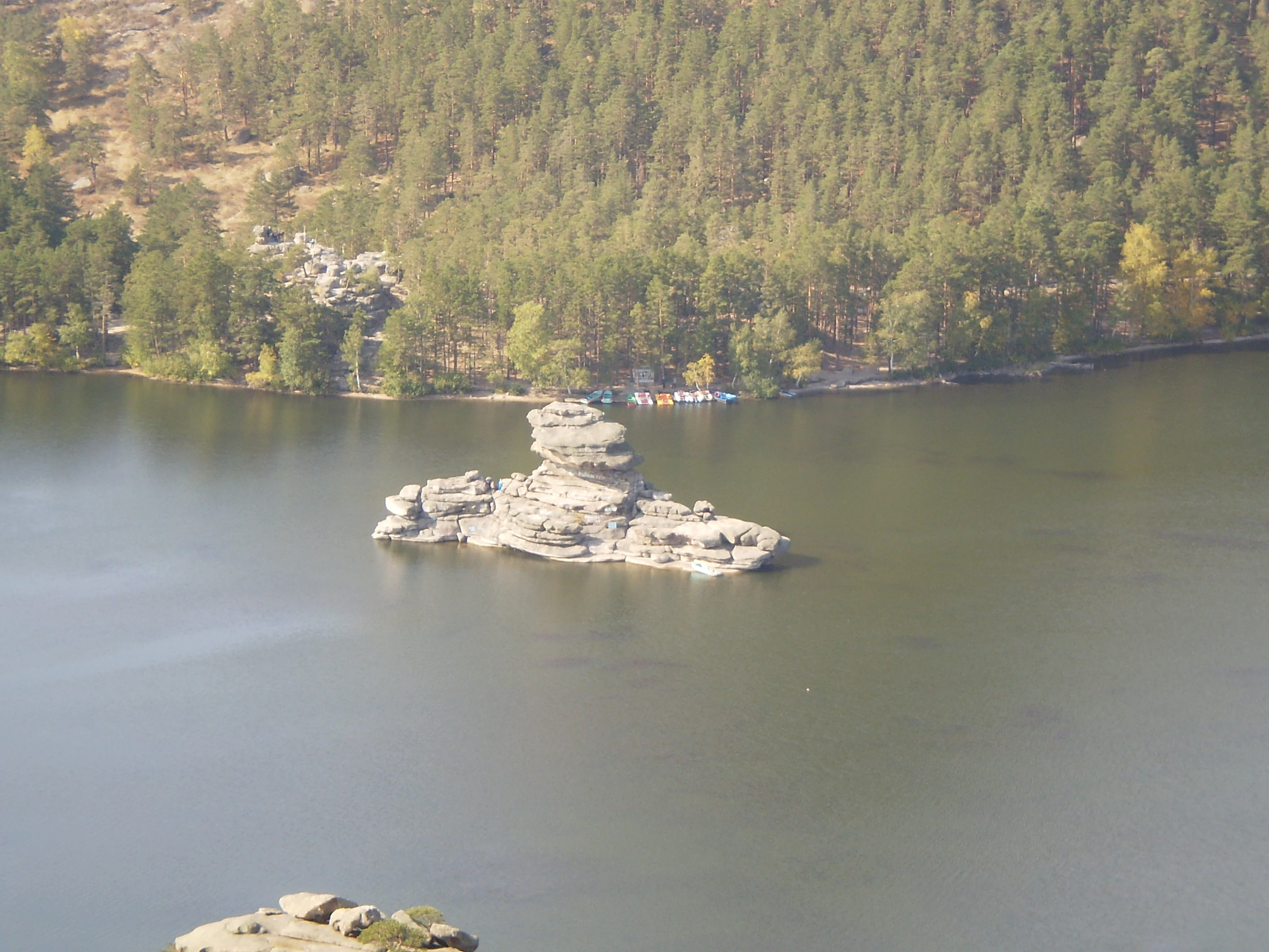 A calm lake with a rocky island in the center, surrounded by forested hills