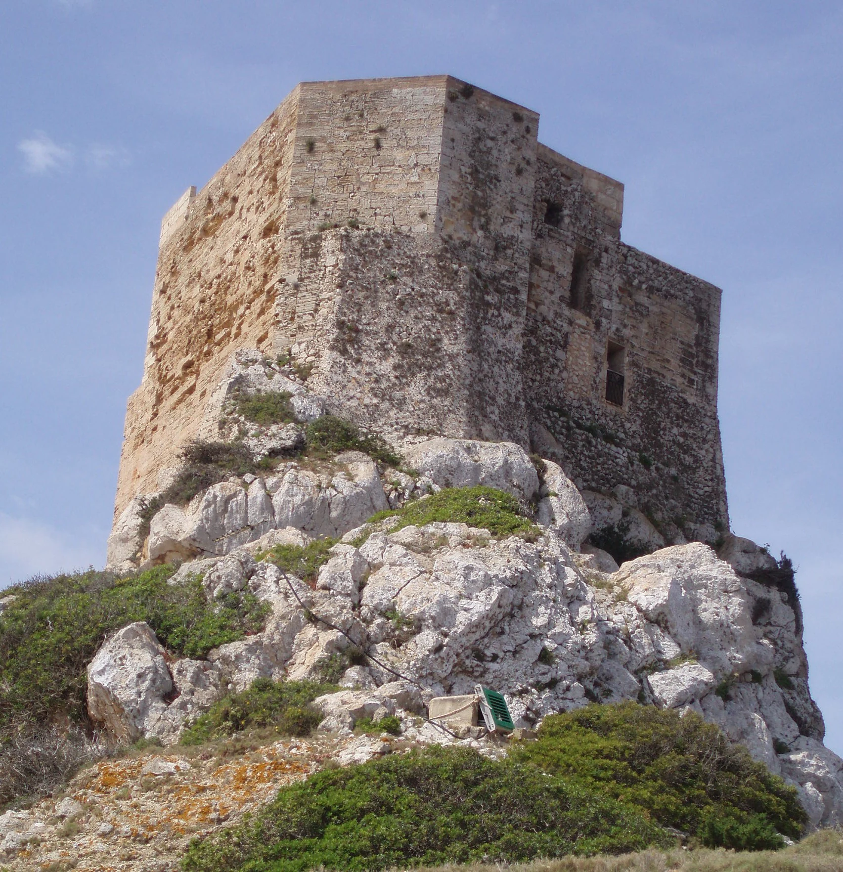 Stone castle on rocky hillside with green vegetation under clear blue sky