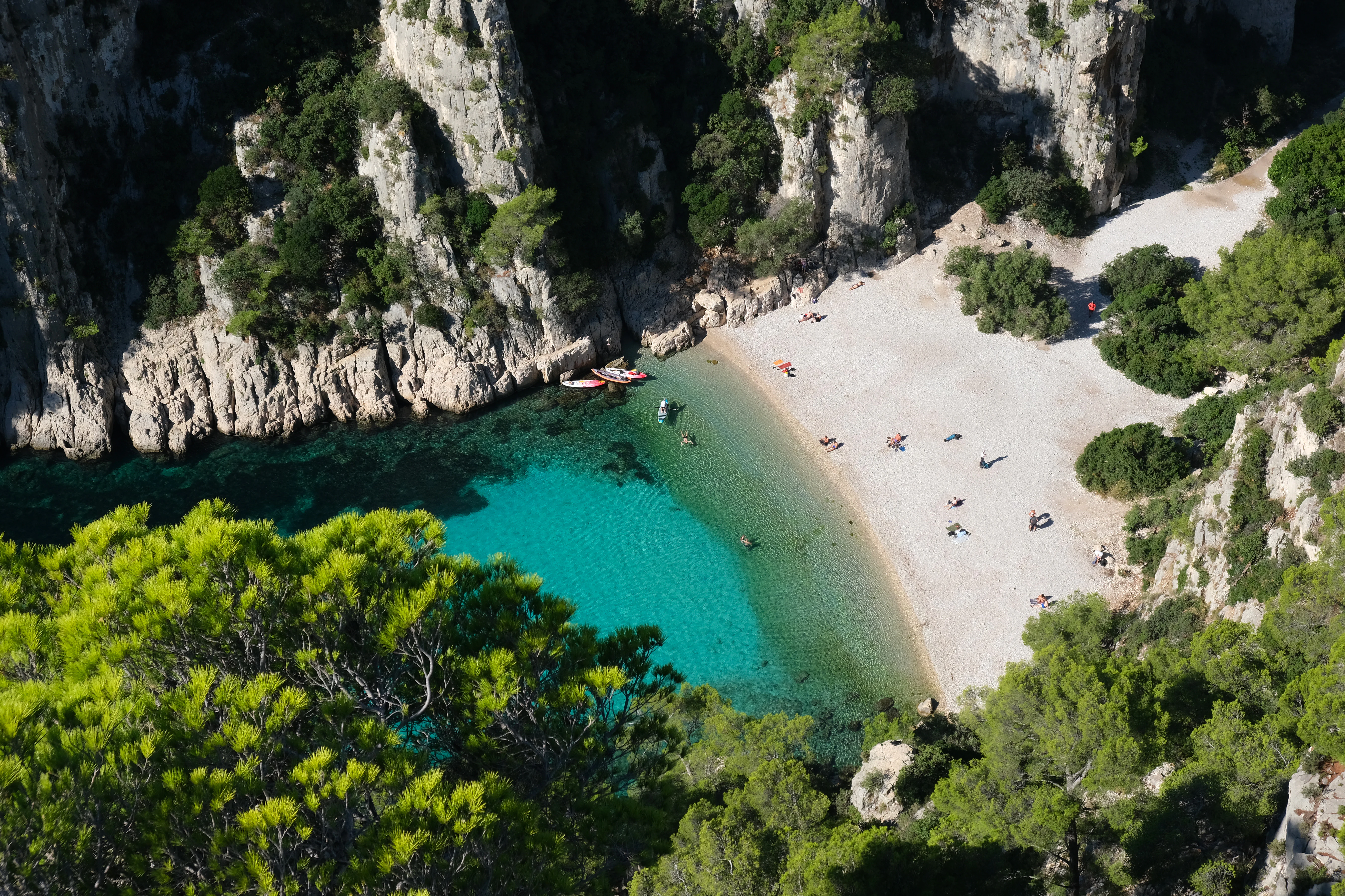 Aerial view of En-Vau calanque beach with turquoise water, sandy shore, rocky cliffs, and green vegetation