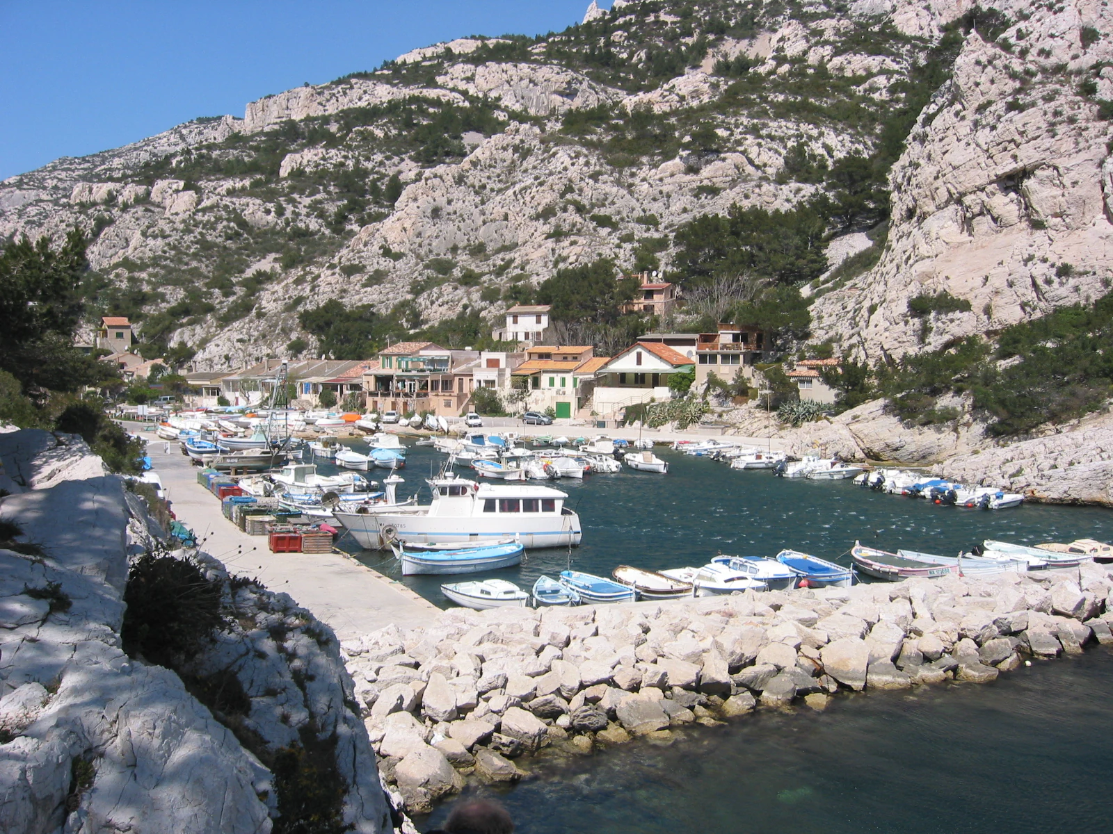 Boats docked in a rocky calanque with limestone cliffs and buildings in the background