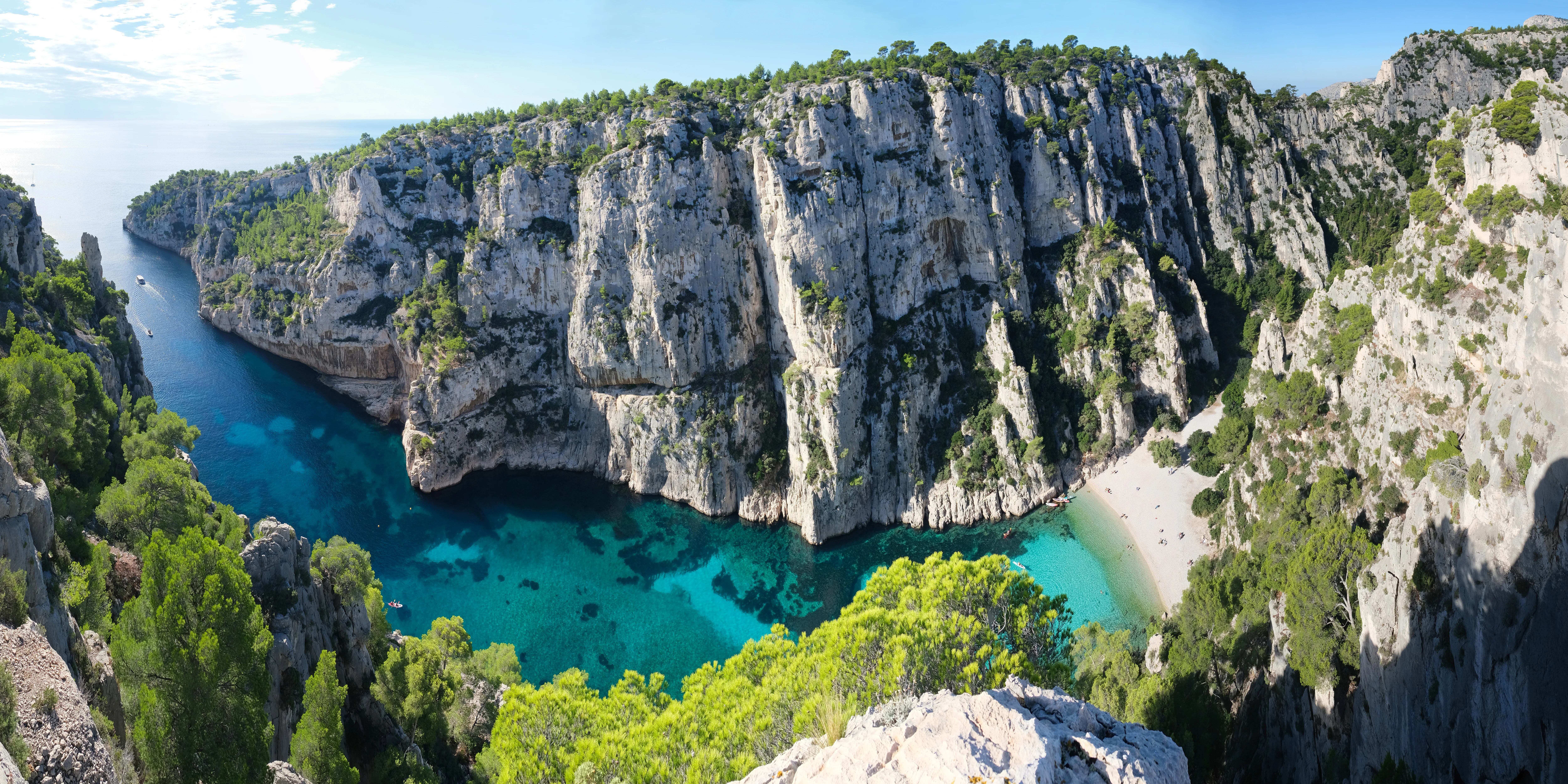 Panoramic view of a calanque with turquoise water surrounded by steep limestone cliffs and green vegetation