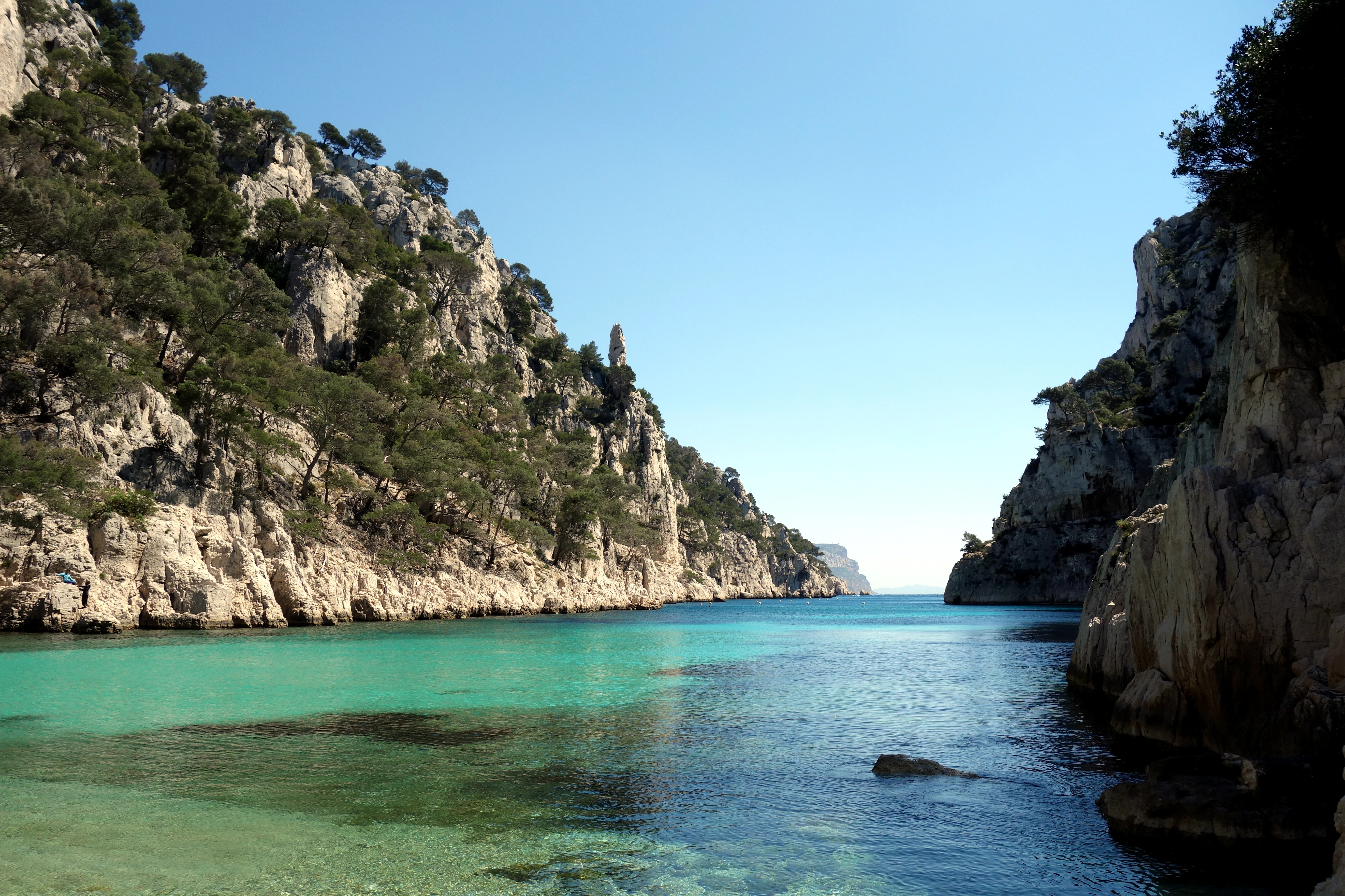 Limestone cliffs on both sides of a narrow turquoise inlet under a clear blue sky