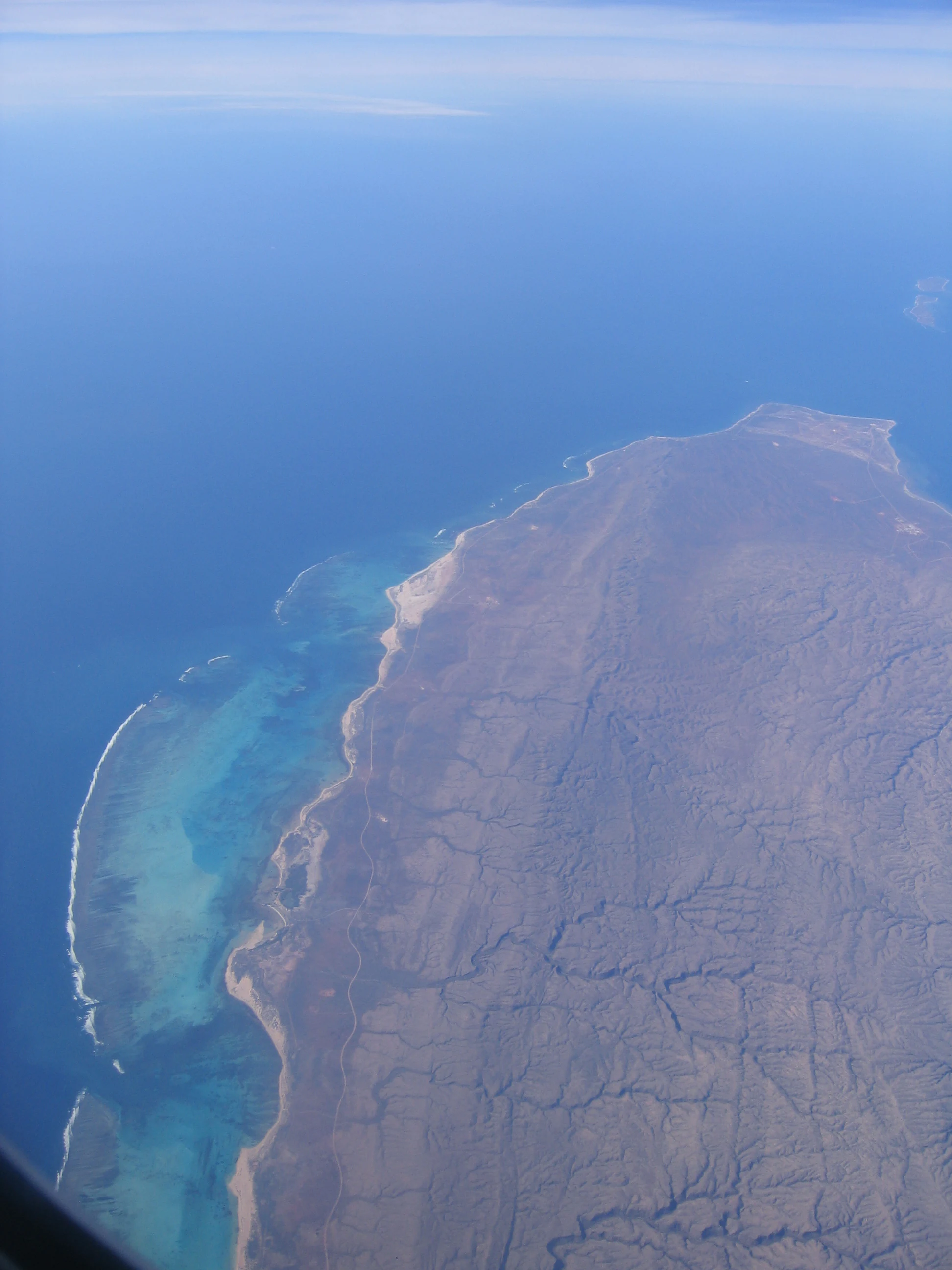 Aerial view showing a coastal peninsula with rugged terrain adjacent to turquoise and deep blue ocean waters