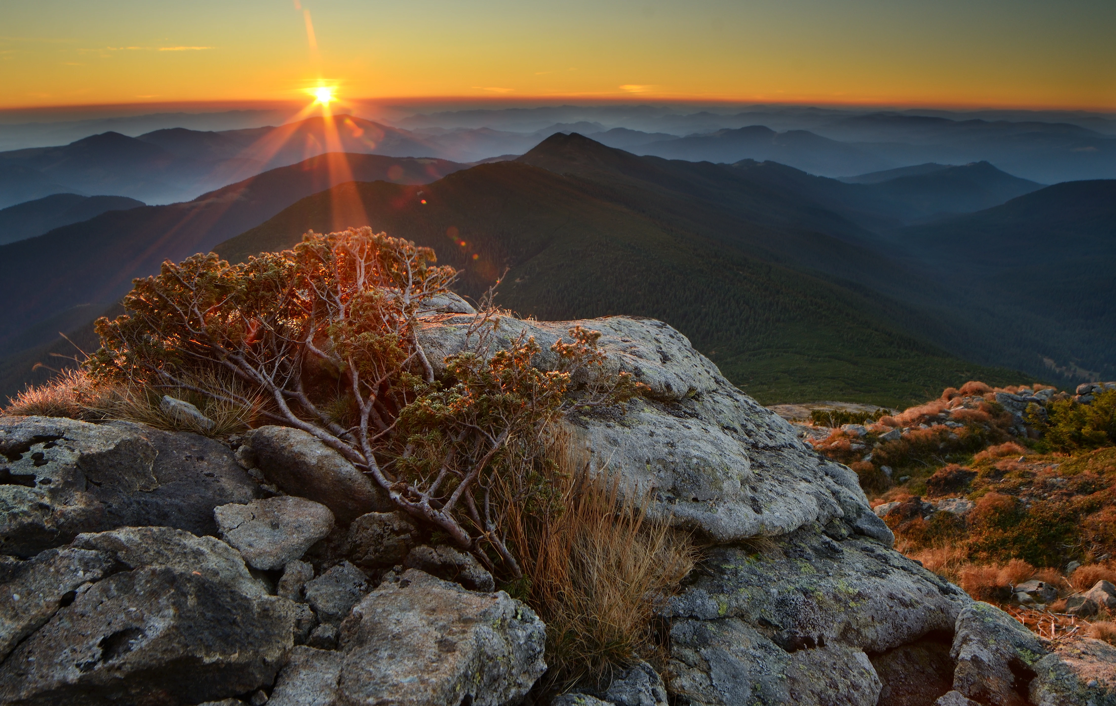Sunrise over rocky mountain peaks with sparse vegetation and distant ridges