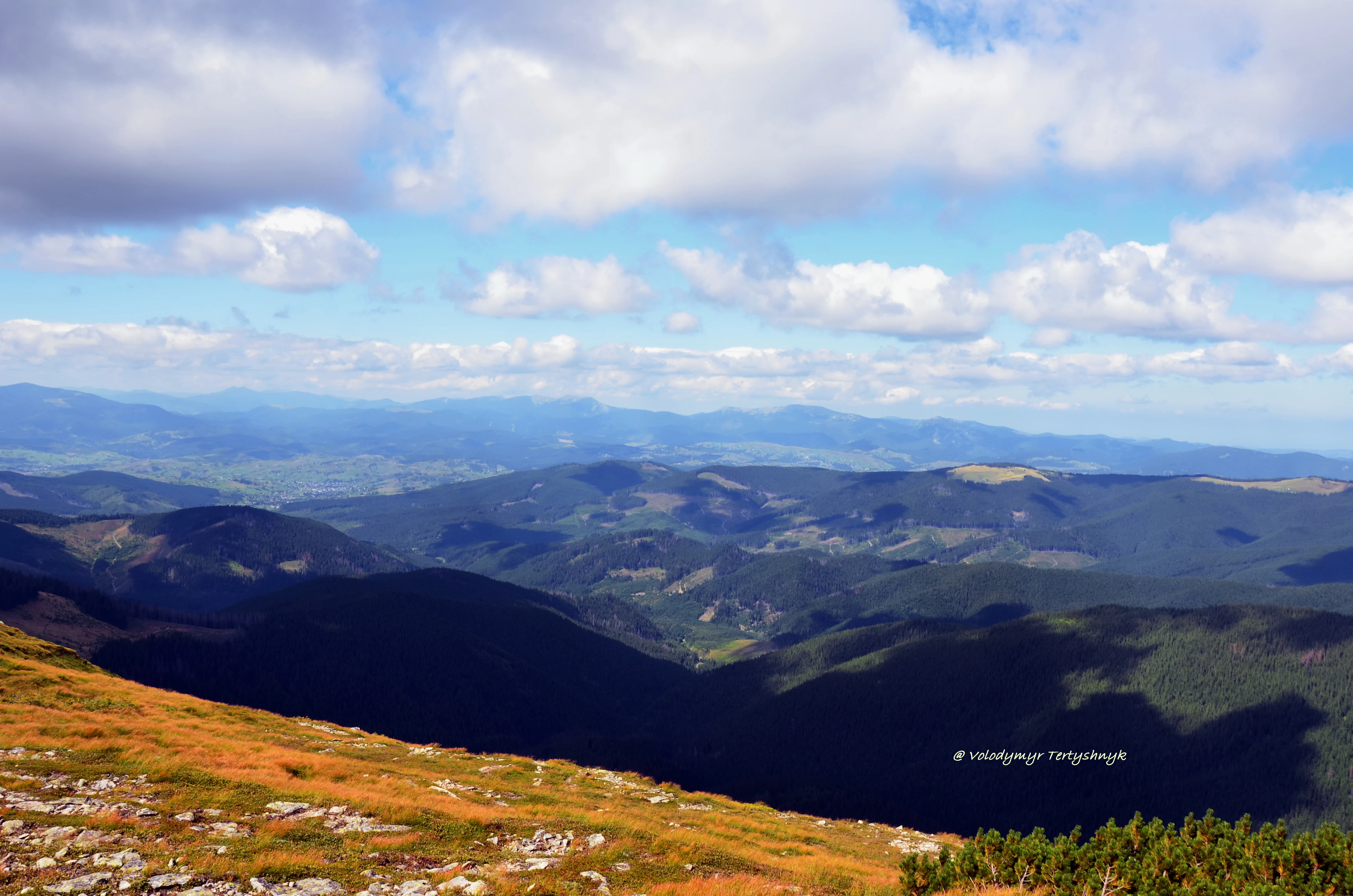 Panoramic view of mountain ranges with valleys and forested slopes under a partly cloudy sky