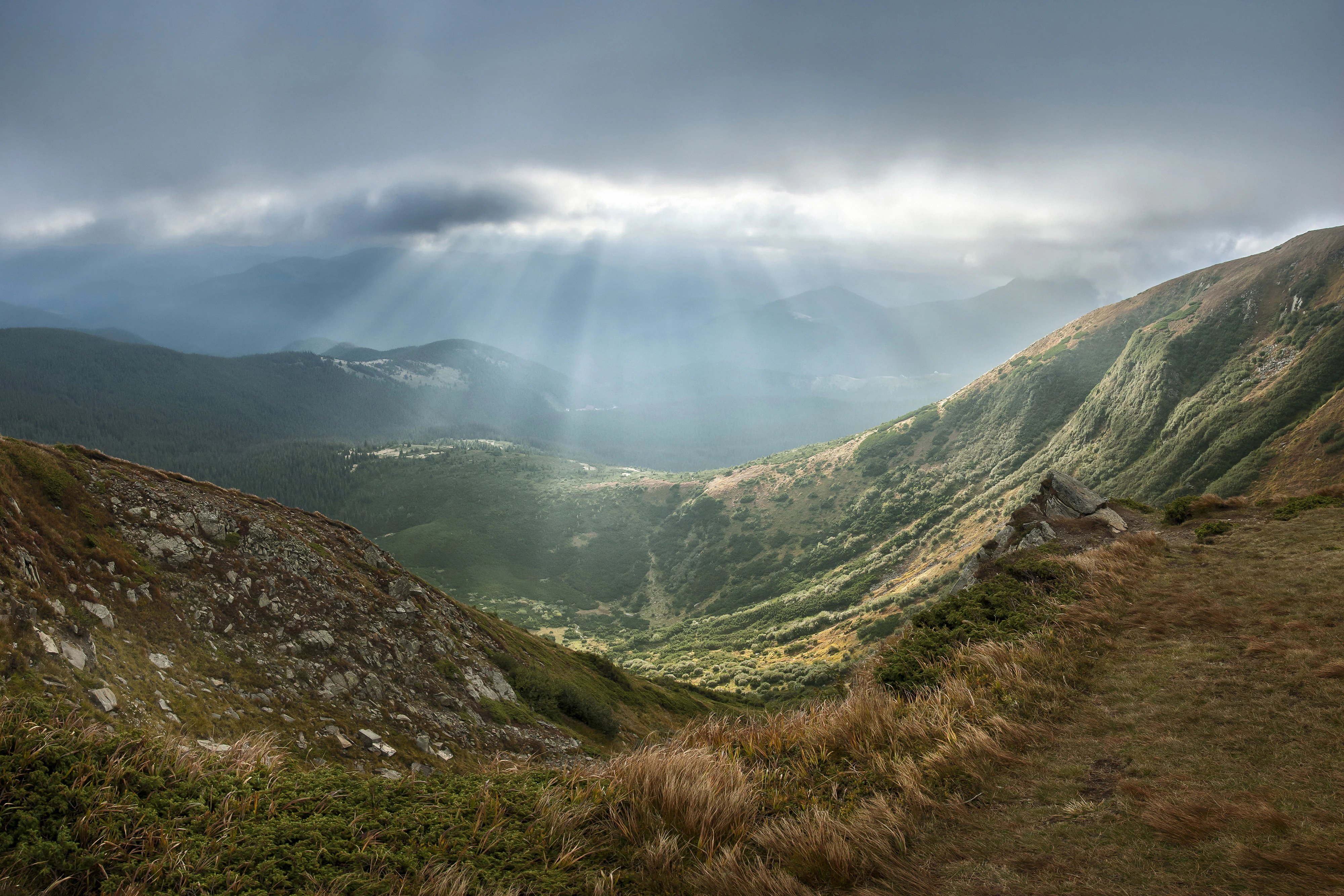 Mountain landscape with valleys, hills, and sunlight rays breaking through clouds