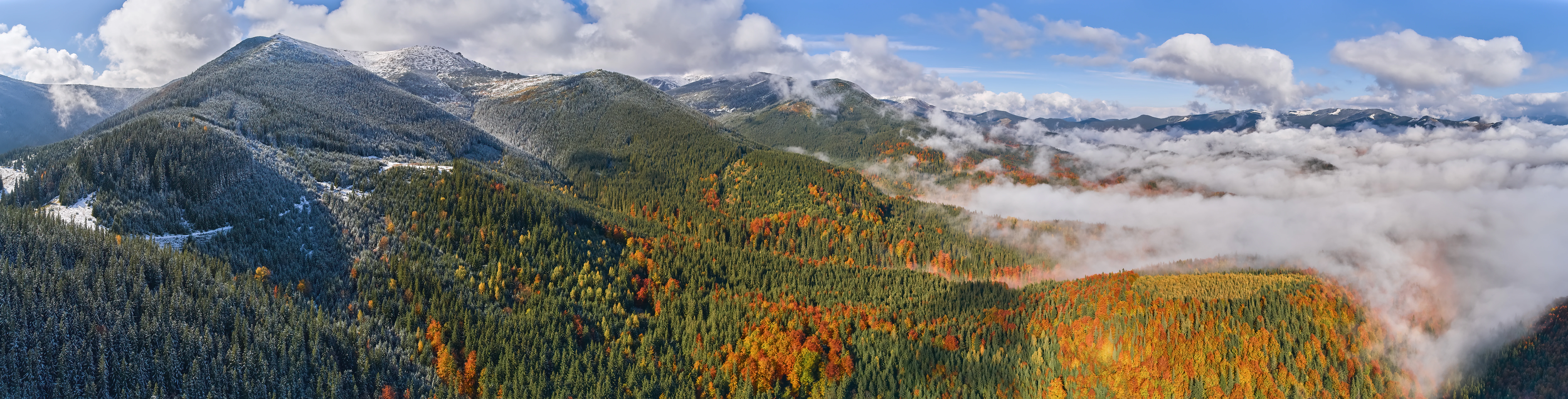 Panoramic landscape of Carpathian National Nature Park with mountain peaks, autumn-colored forests, and low-lying clouds