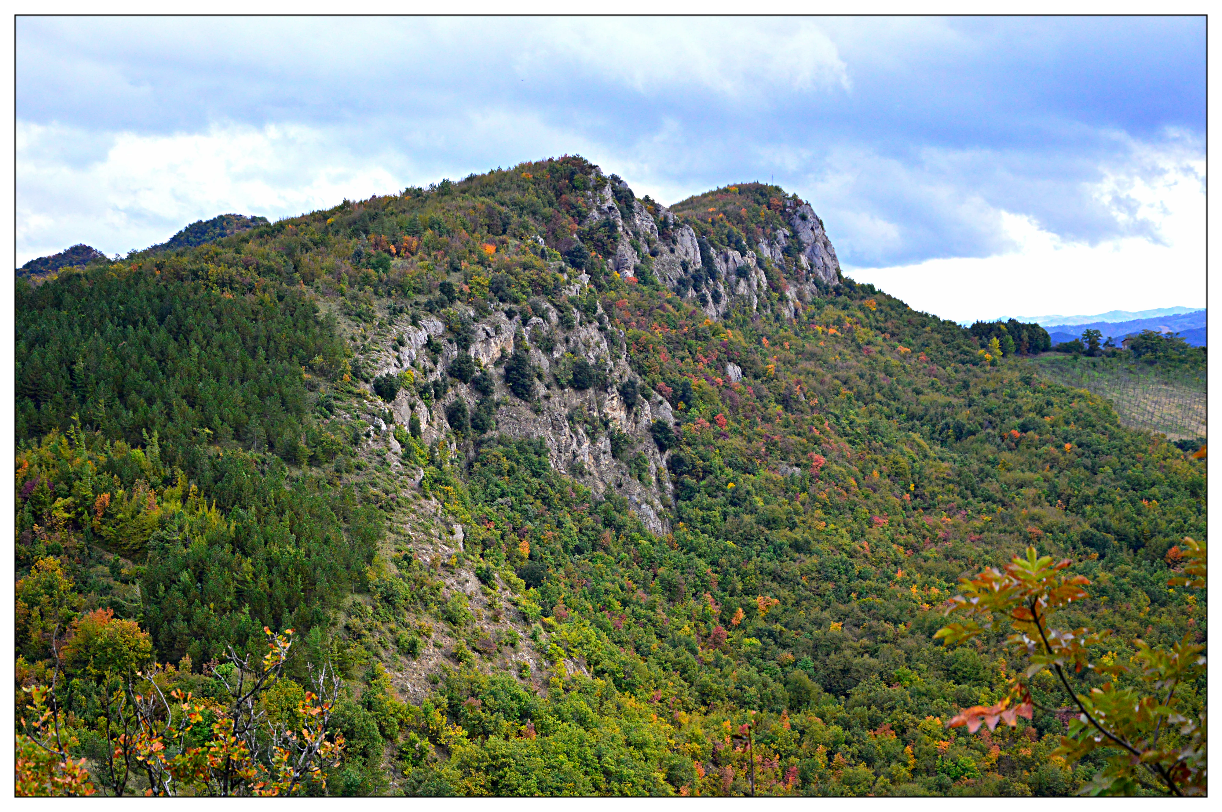 A landscape view of a hilly, forested ridge showing exposed rocky gypsum cliffs under a cloudy sky.