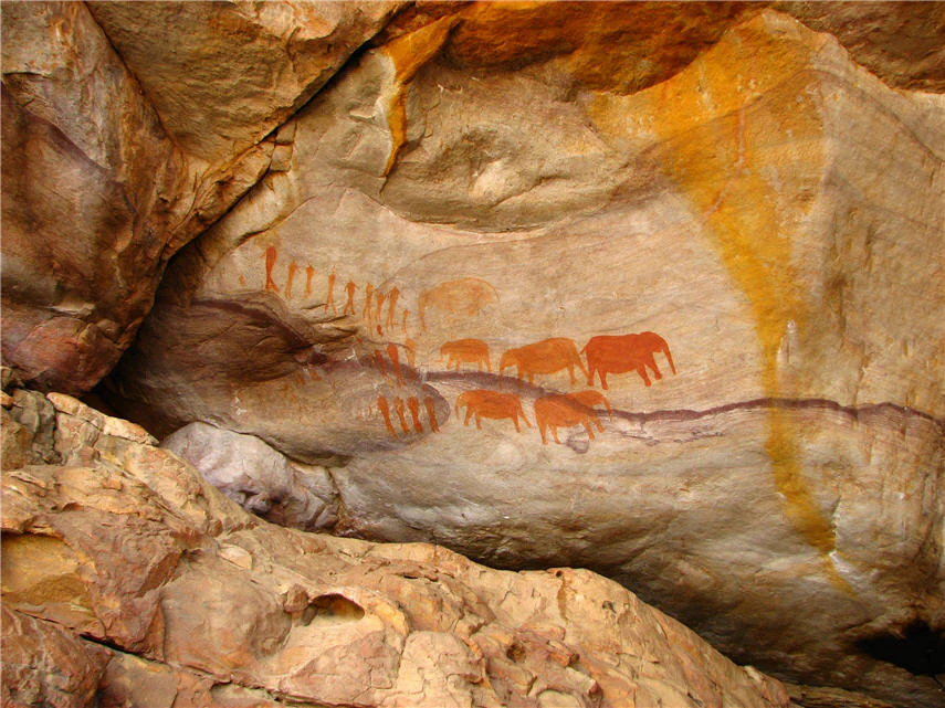 Ancient ochre-colored cave paintings of animals and human figures on a rugged sandstone rock face.