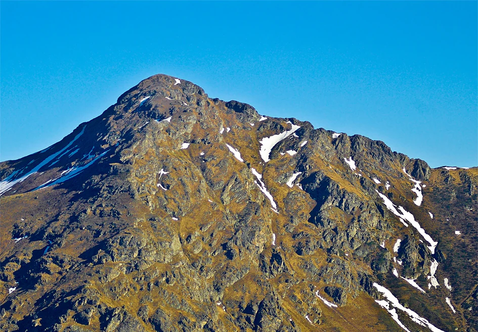 Rugged mountain peak with patches of snow under clear blue sky