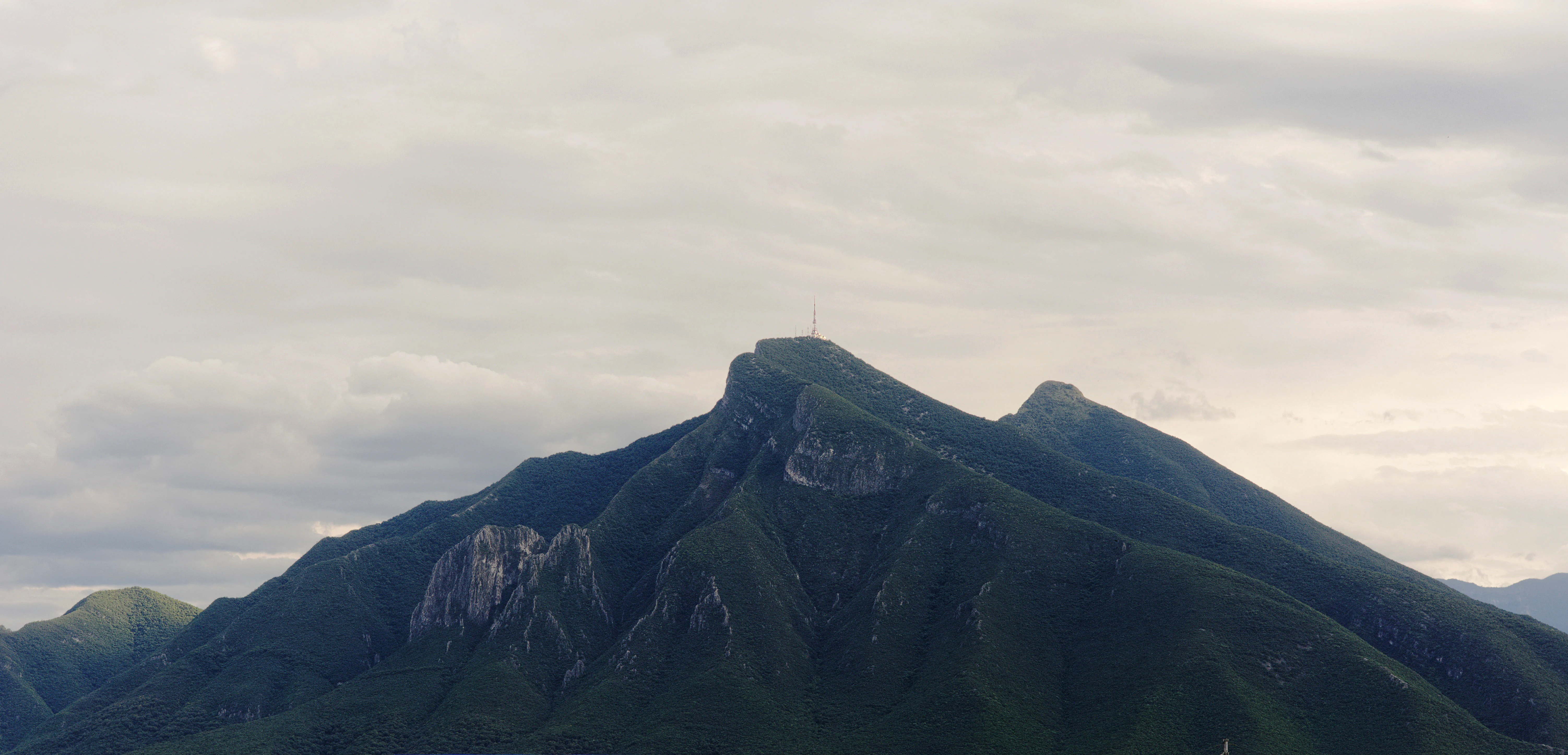 A wide view of the prominent, rugged peak of Cerro de la Silla mountain under a cloudy sky.
