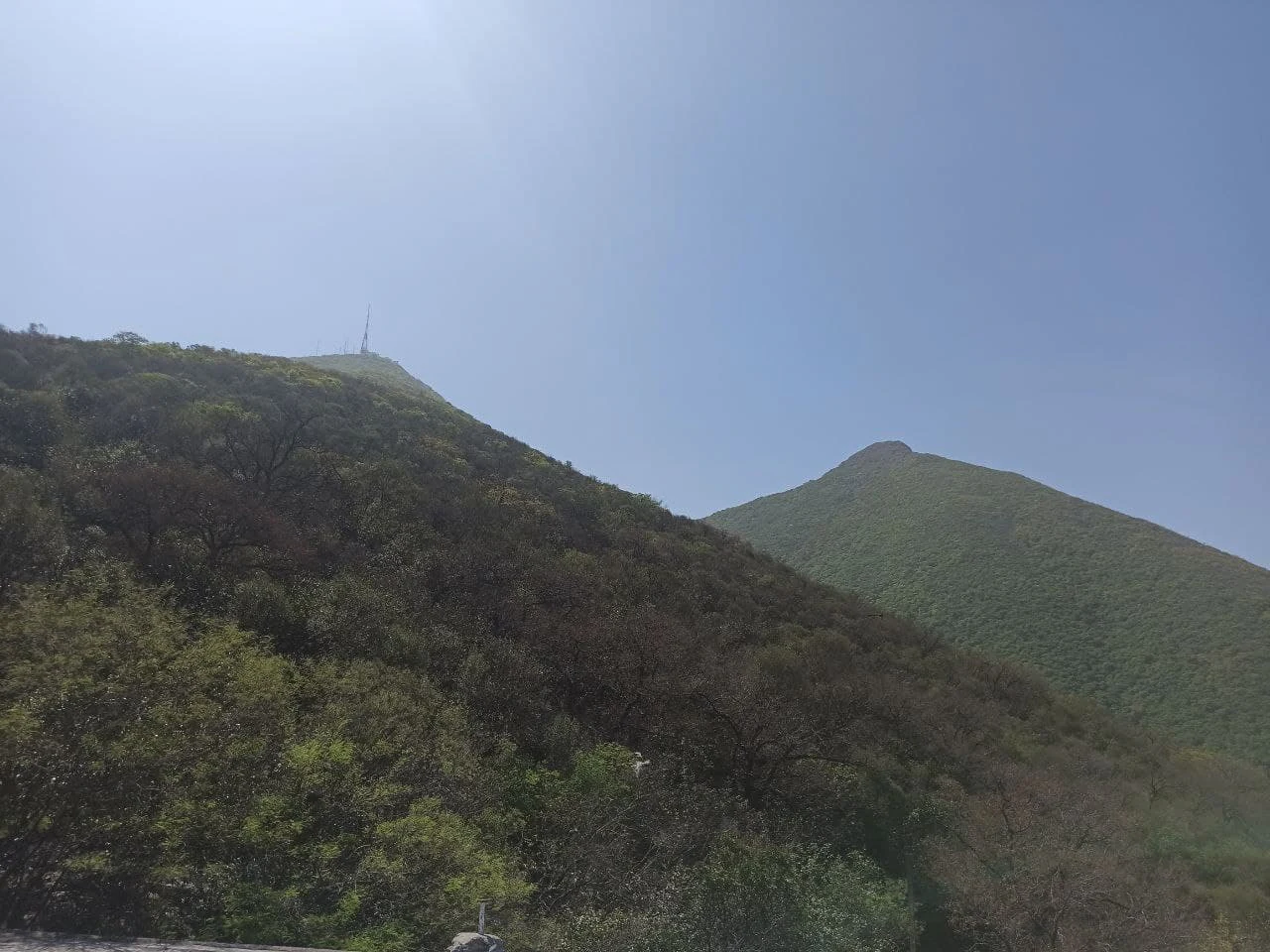 A wide angle view of the green, shrub-covered slopes and rocky summits of Cerro de la Silla in Mexico against a bright, clear blue sky.