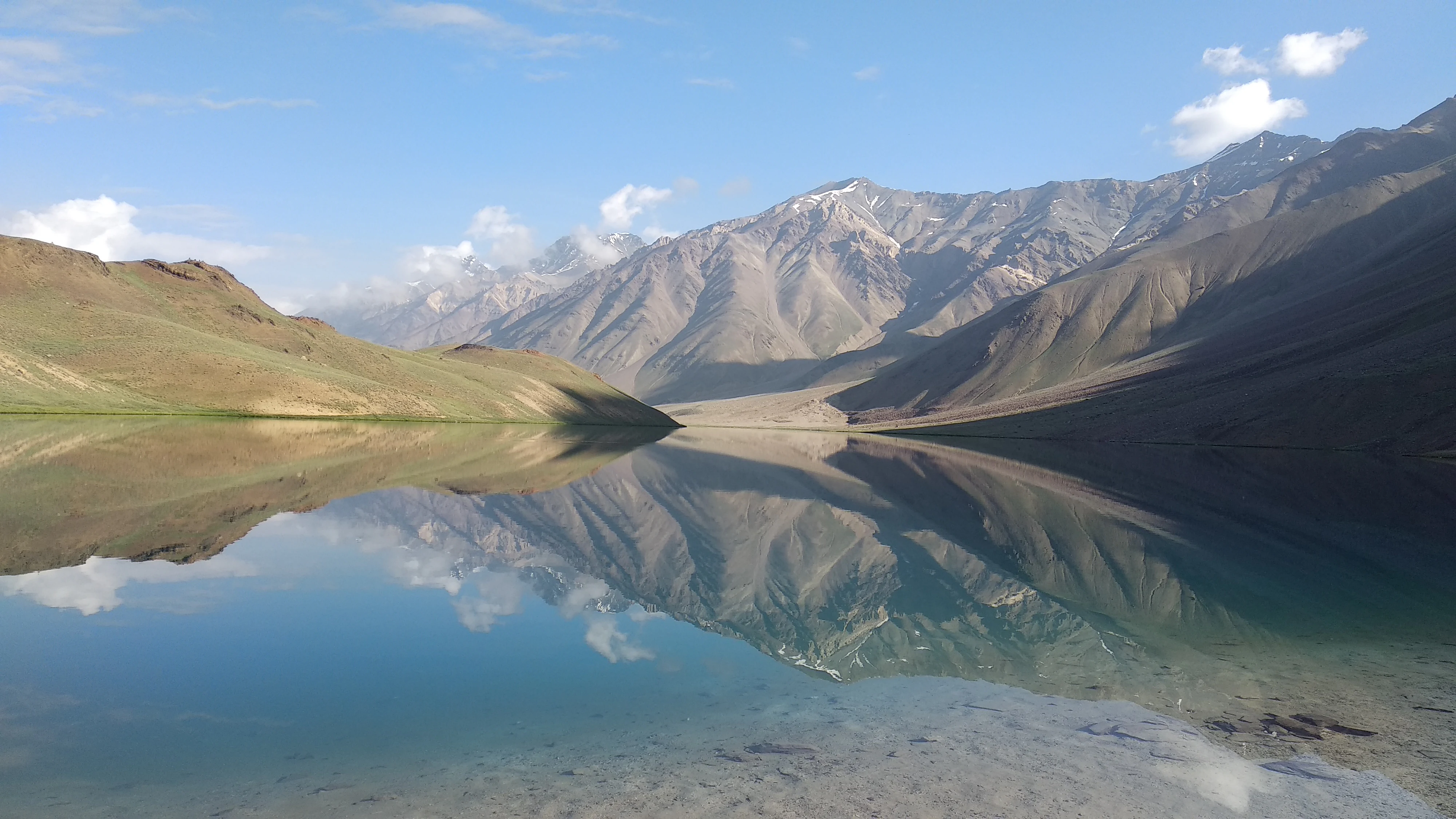 A wide, eye-level shot of a calm lake in the mountains, with a perfect reflection of the surrounding rocky slopes and sky on the water surface.
