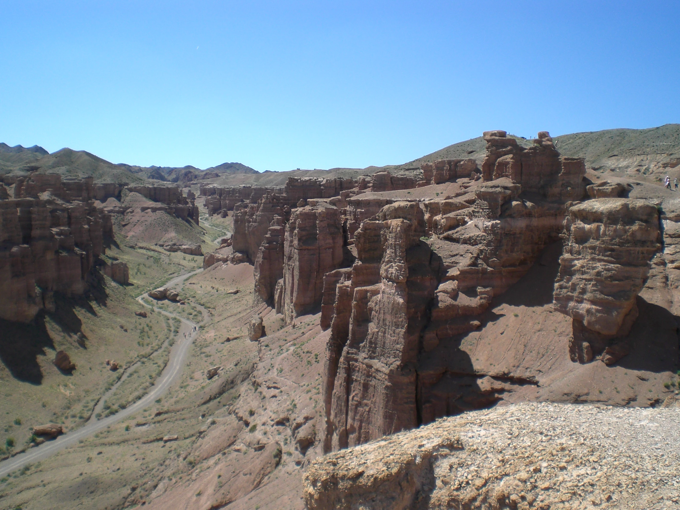 Winding road through rugged canyon landscape with red rock formations under clear blue sky