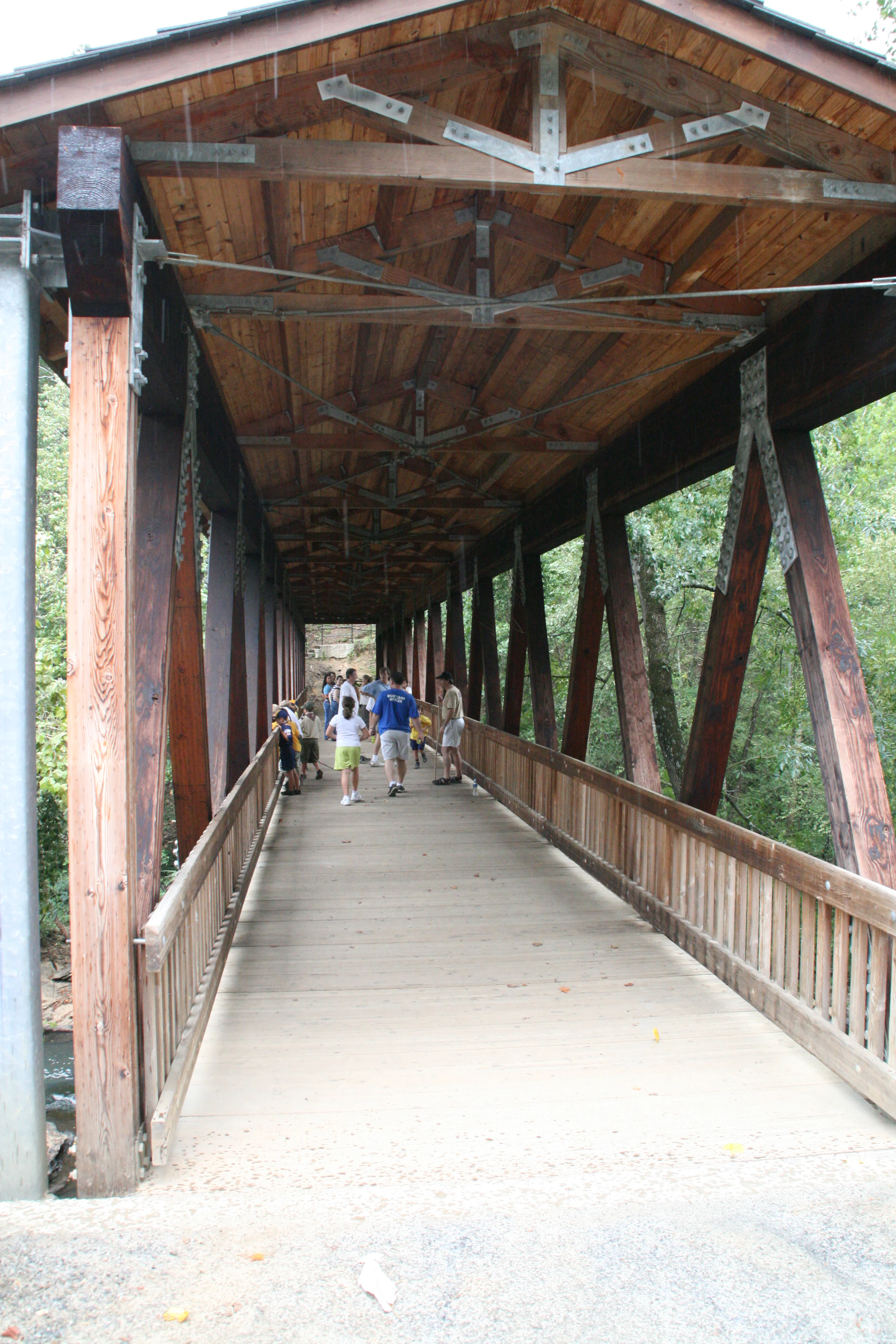 A group of people walks across a wooden covered pedestrian bridge with exposed timber framework.