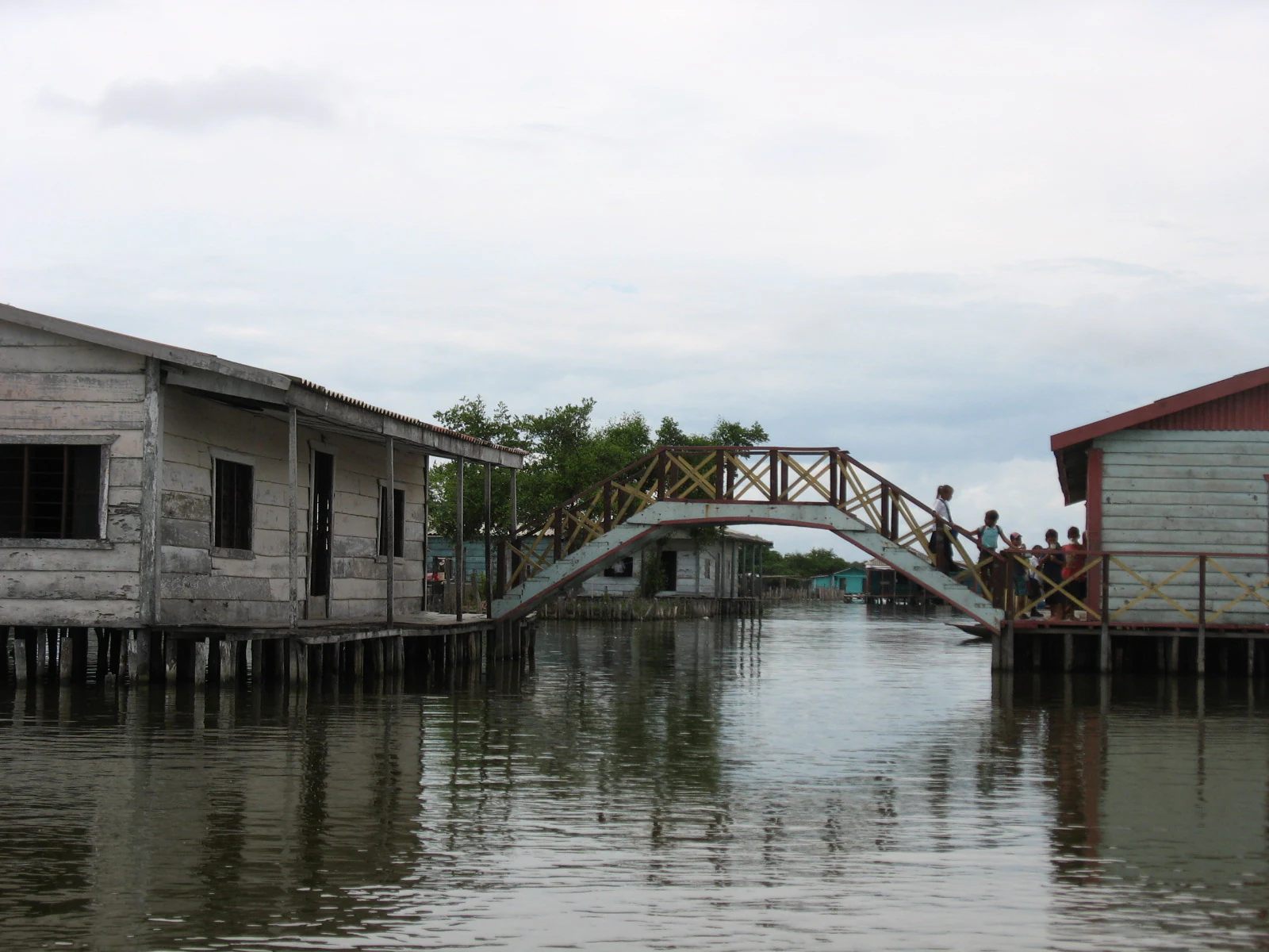Wooden bridge connecting stilt houses built over water with people walking on the bridge