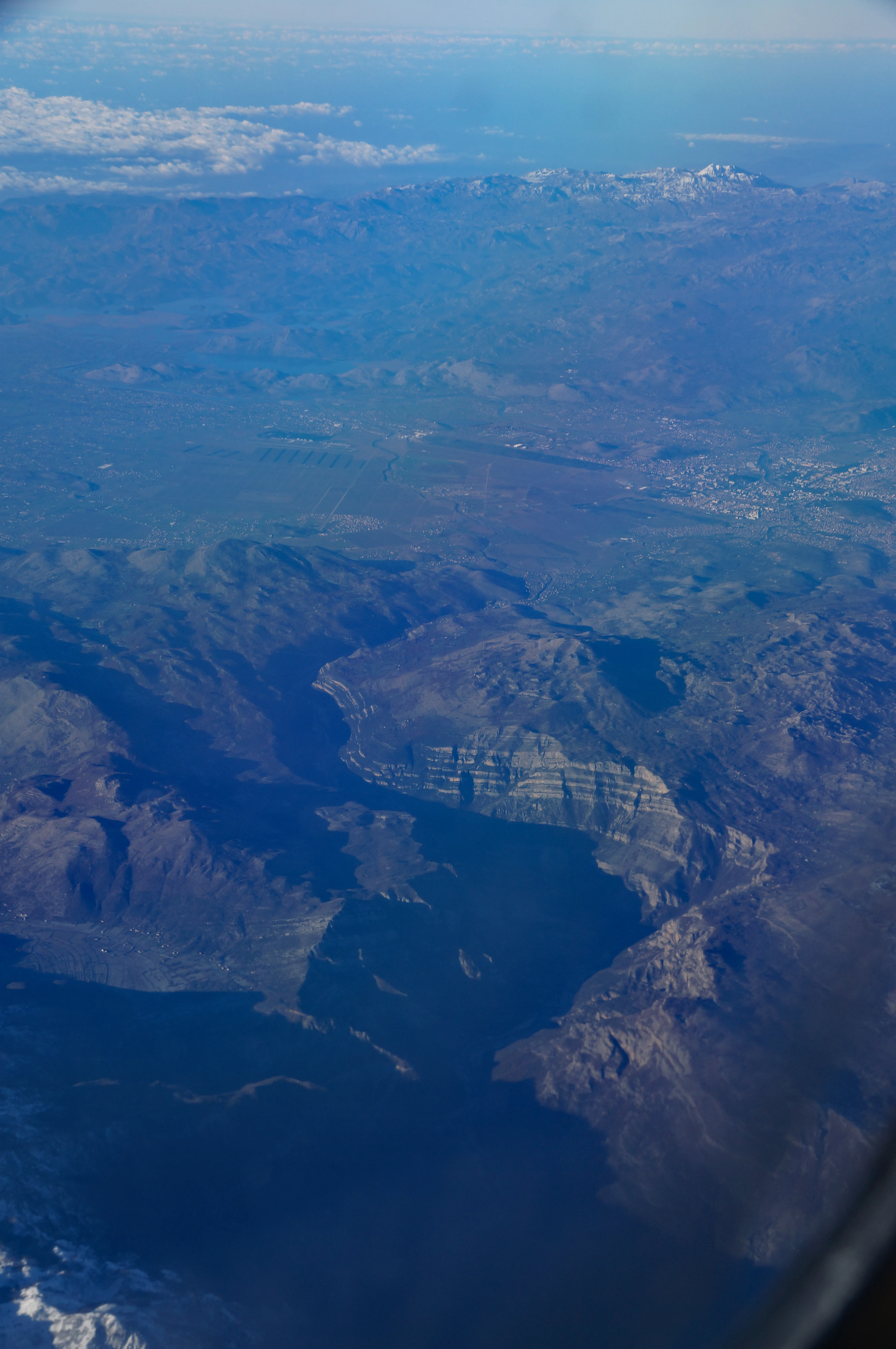 An aerial view from an airplane window looking down at the Cem Valley, showing a deep river canyon winding through mountainous terrain with snowy peaks in the distance.