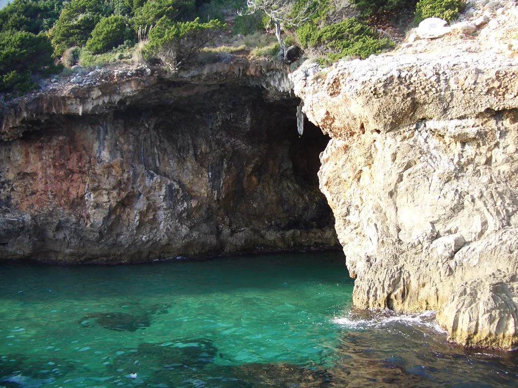 Rocky coastal cave entrance with turquoise water and green vegetation on top of cliffs