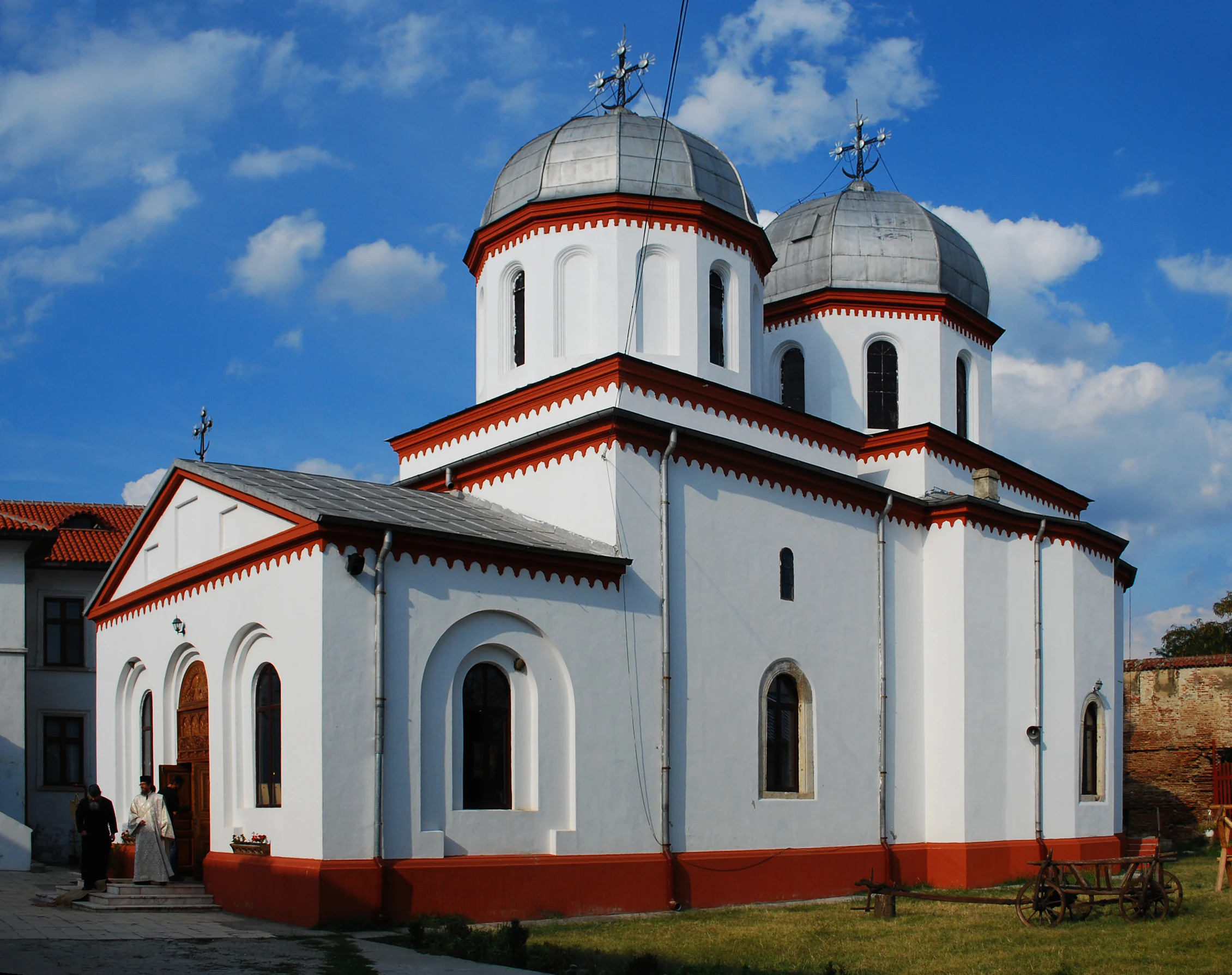 White and red church with two domes, crosses on top, and blue sky with scattered clouds