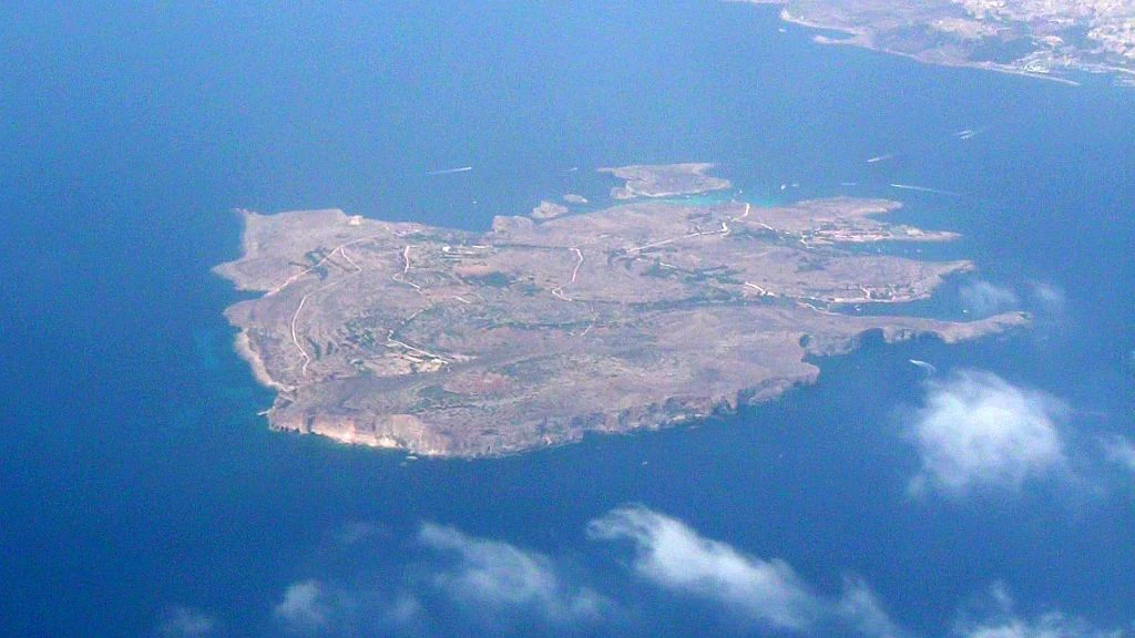 An aerial bird's eye view of the small island of Comino in Malta, surrounded by the deep blue Mediterranean Sea.