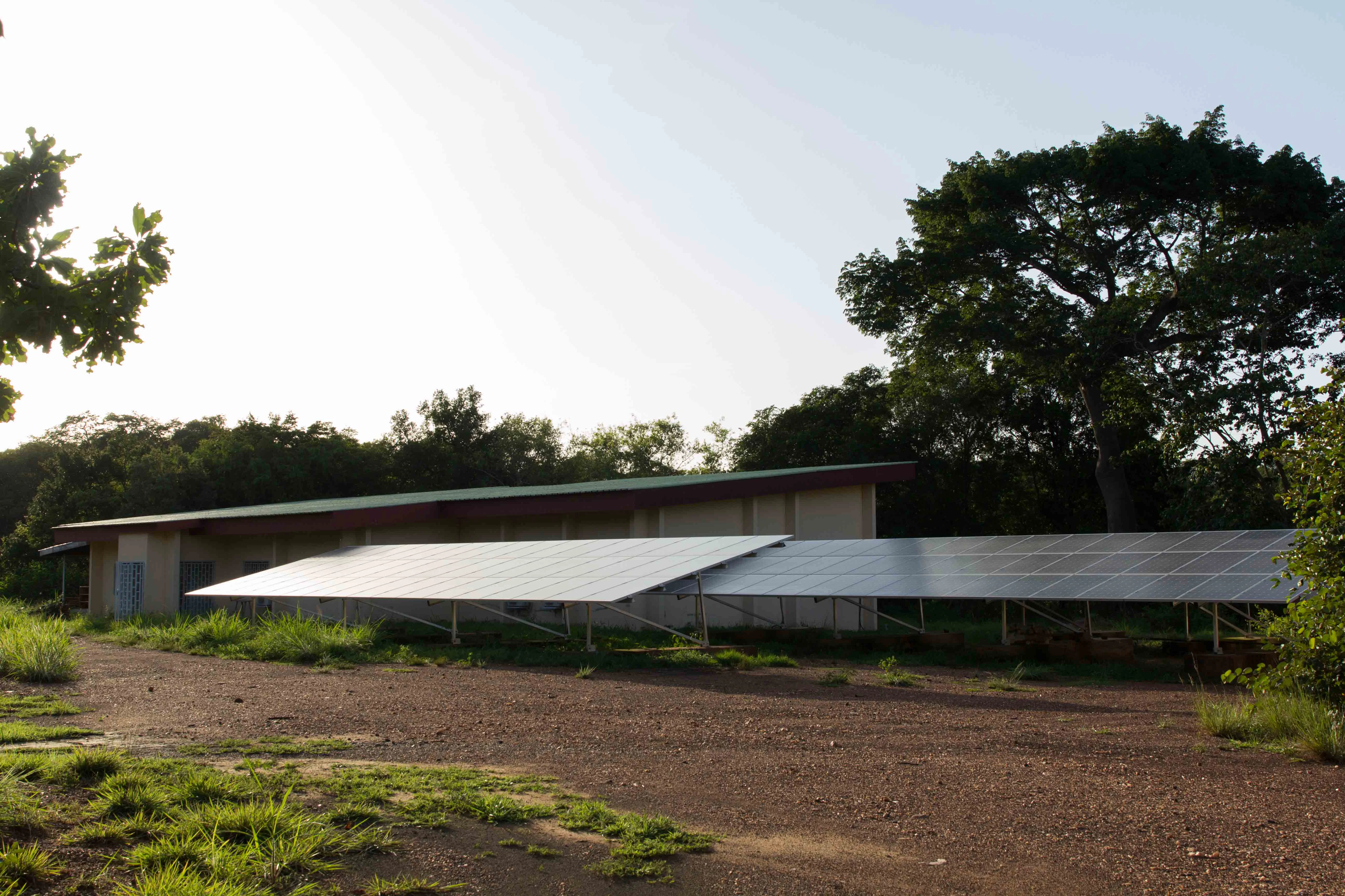 Edificio de estación de investigación con paneles solares en el tejado, rodeado de un paisaje de sabana con árboles y suelo seco