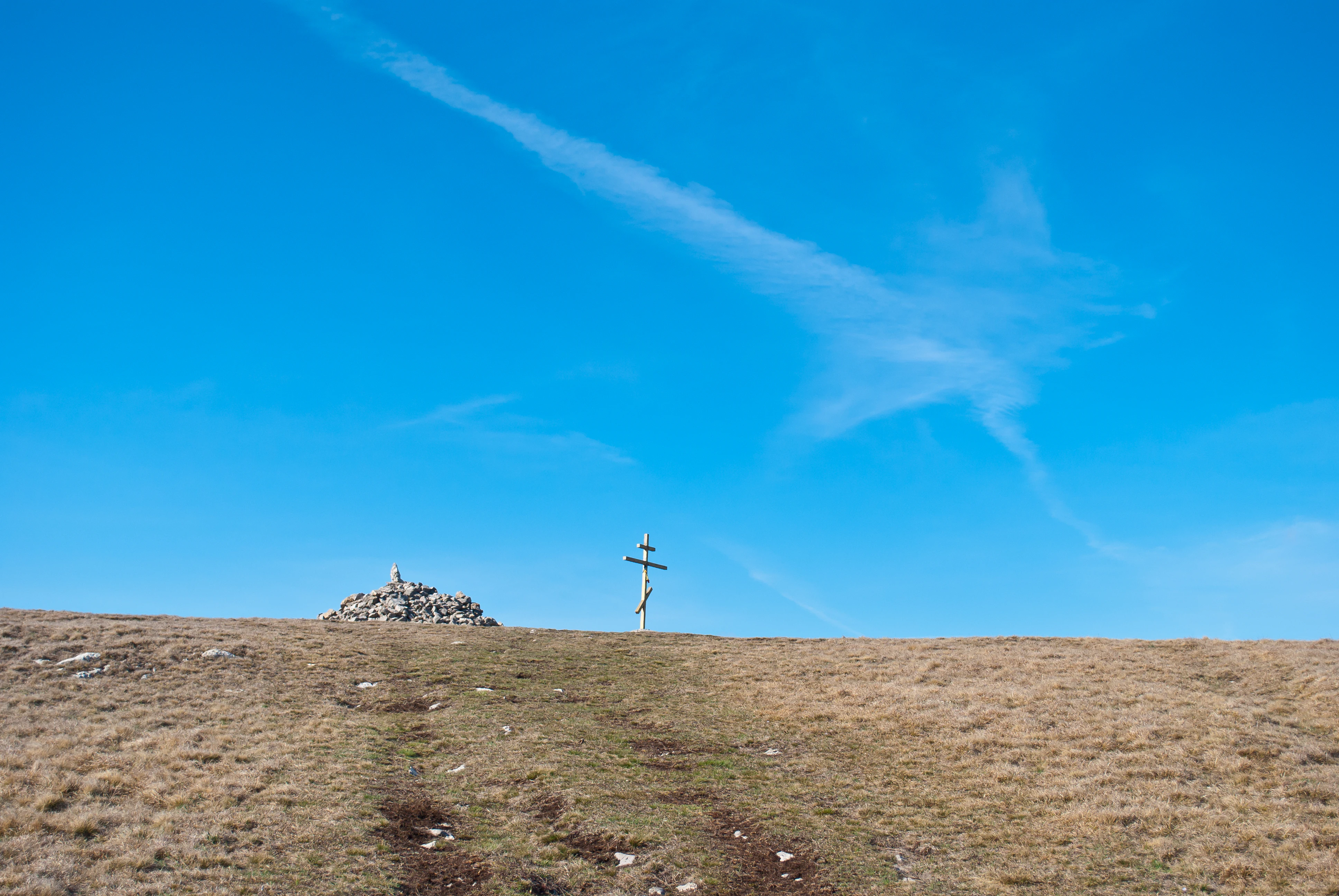 Grassy hilltop with stone cairn and wooden cross under clear blue sky