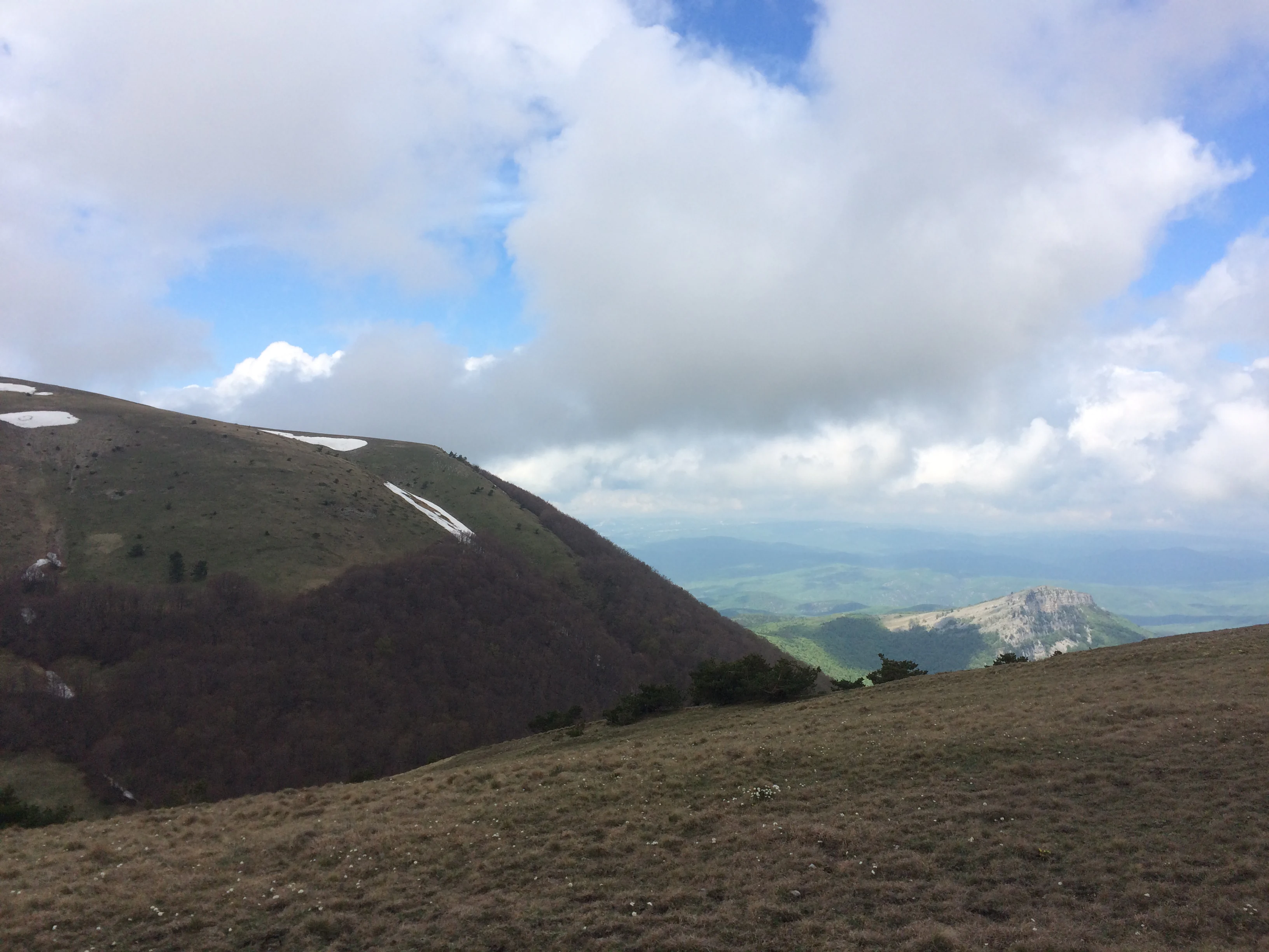 Grassy mountain slopes with patches of snow, blue sky with white clouds