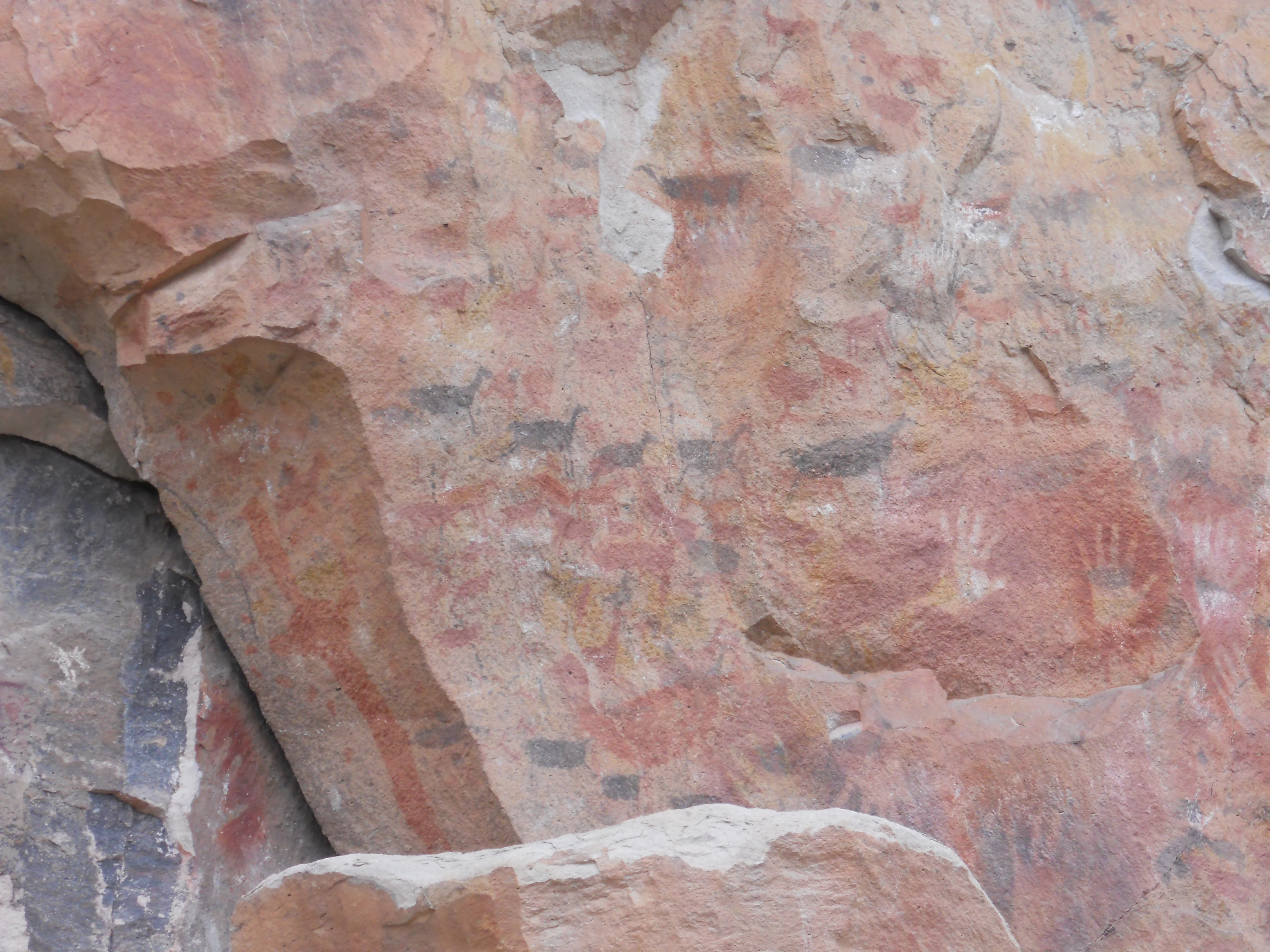 Ancient rock wall featuring faded red and black painted animal figures and hand stencils.