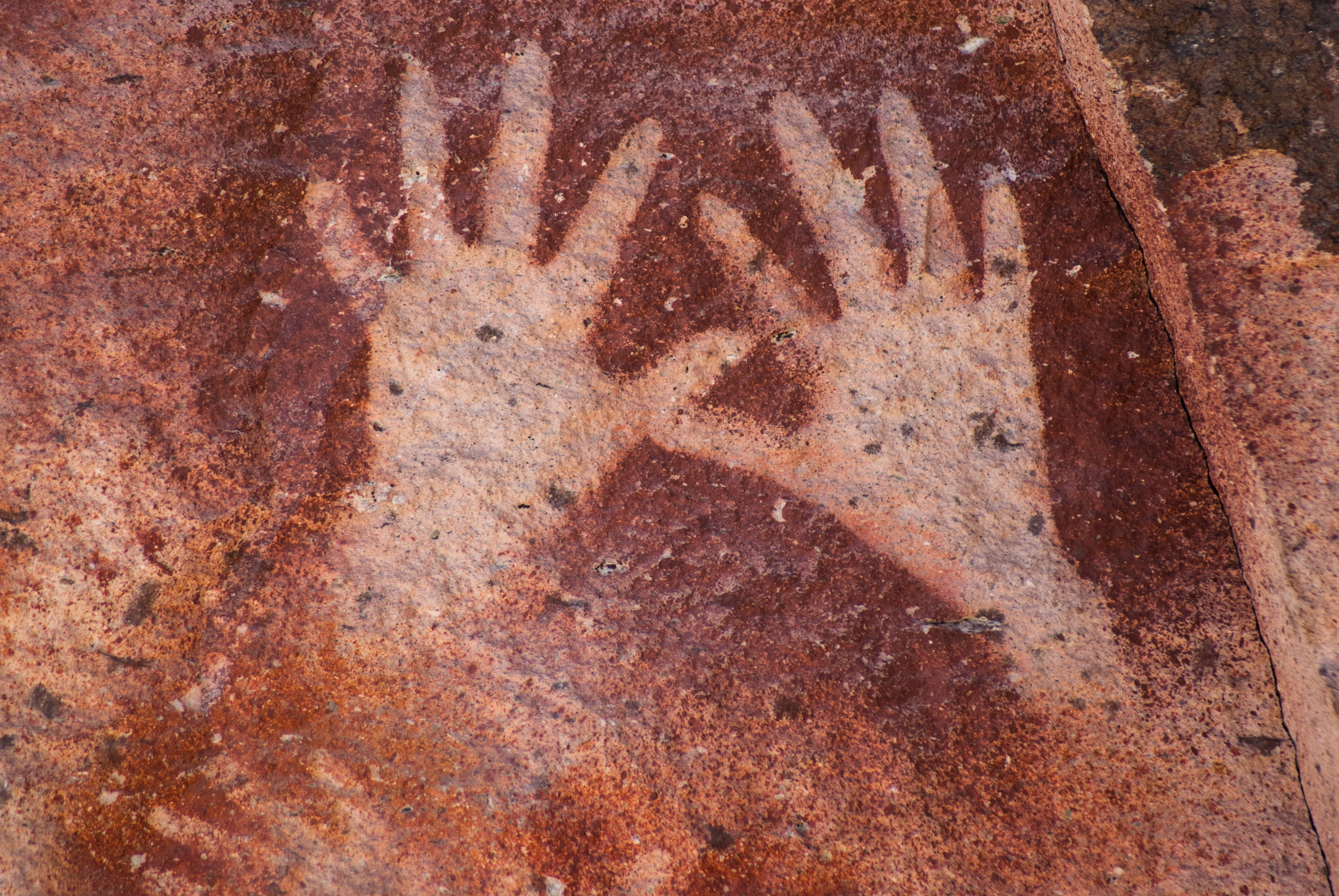 Close-up view of two pale hand stencils painted onto a rough, reddish-brown stone surface.